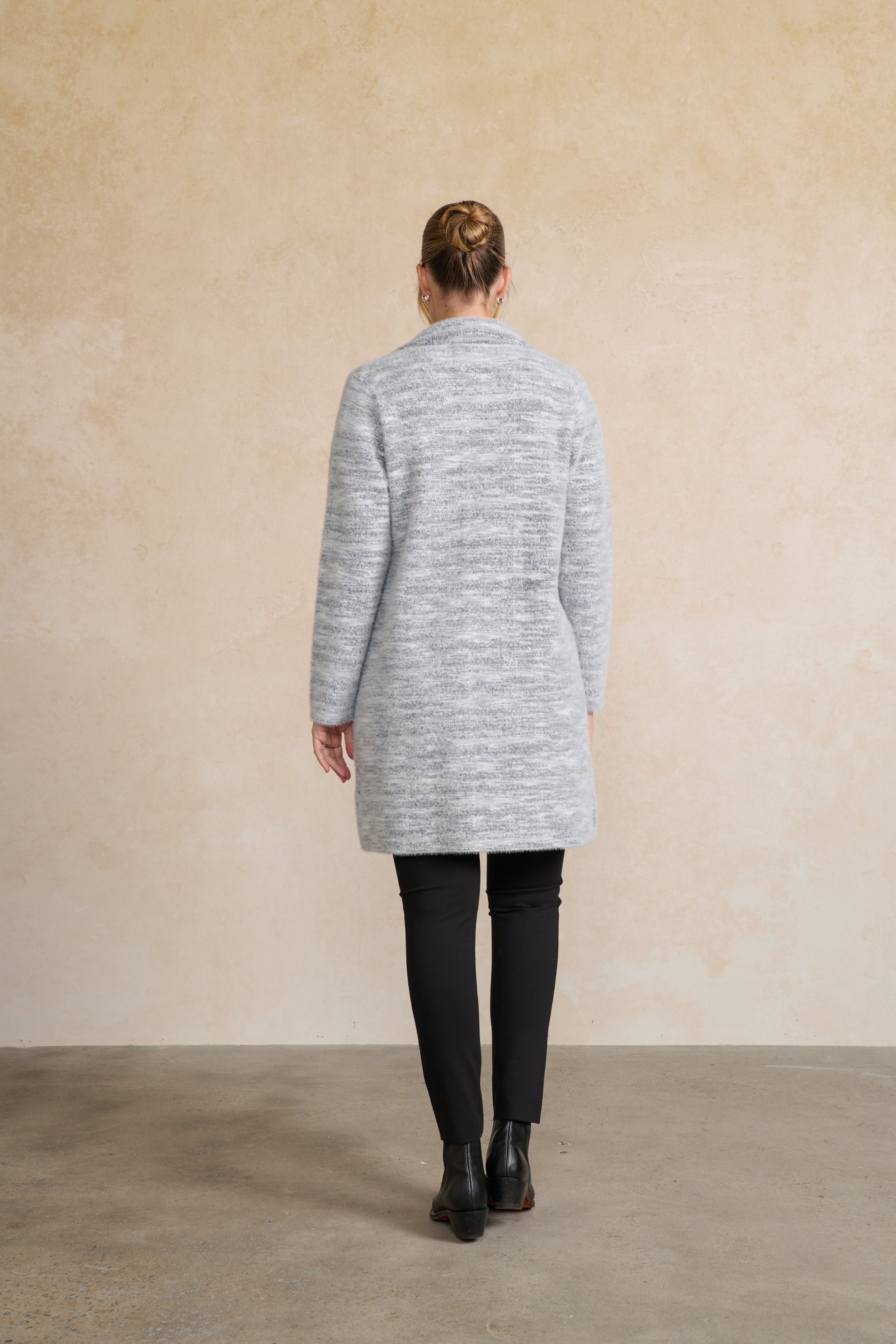 Person wearing a gray cardigan standing against a beige wall back angle