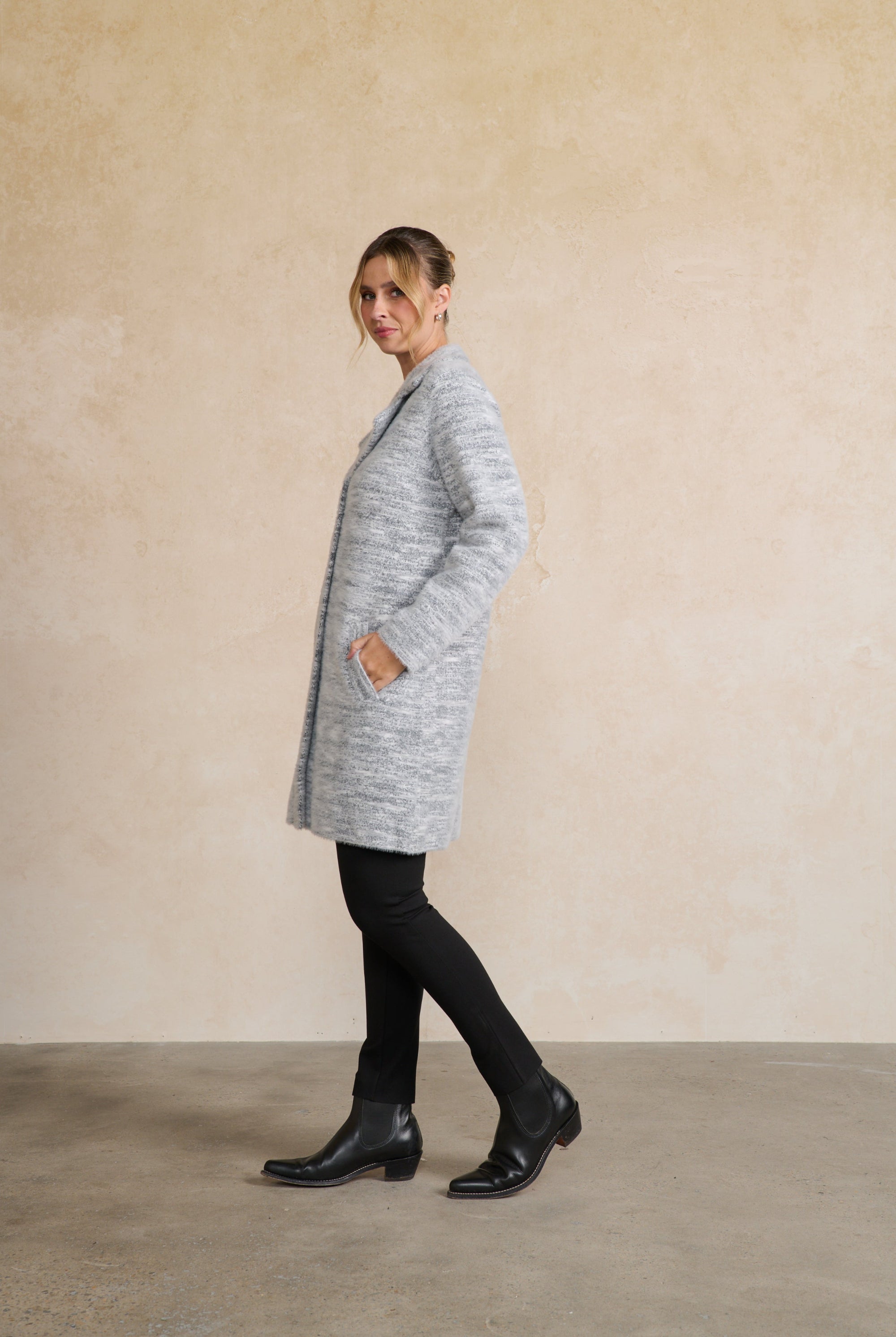 Woman wearing a gray coat standing against a beige wall.