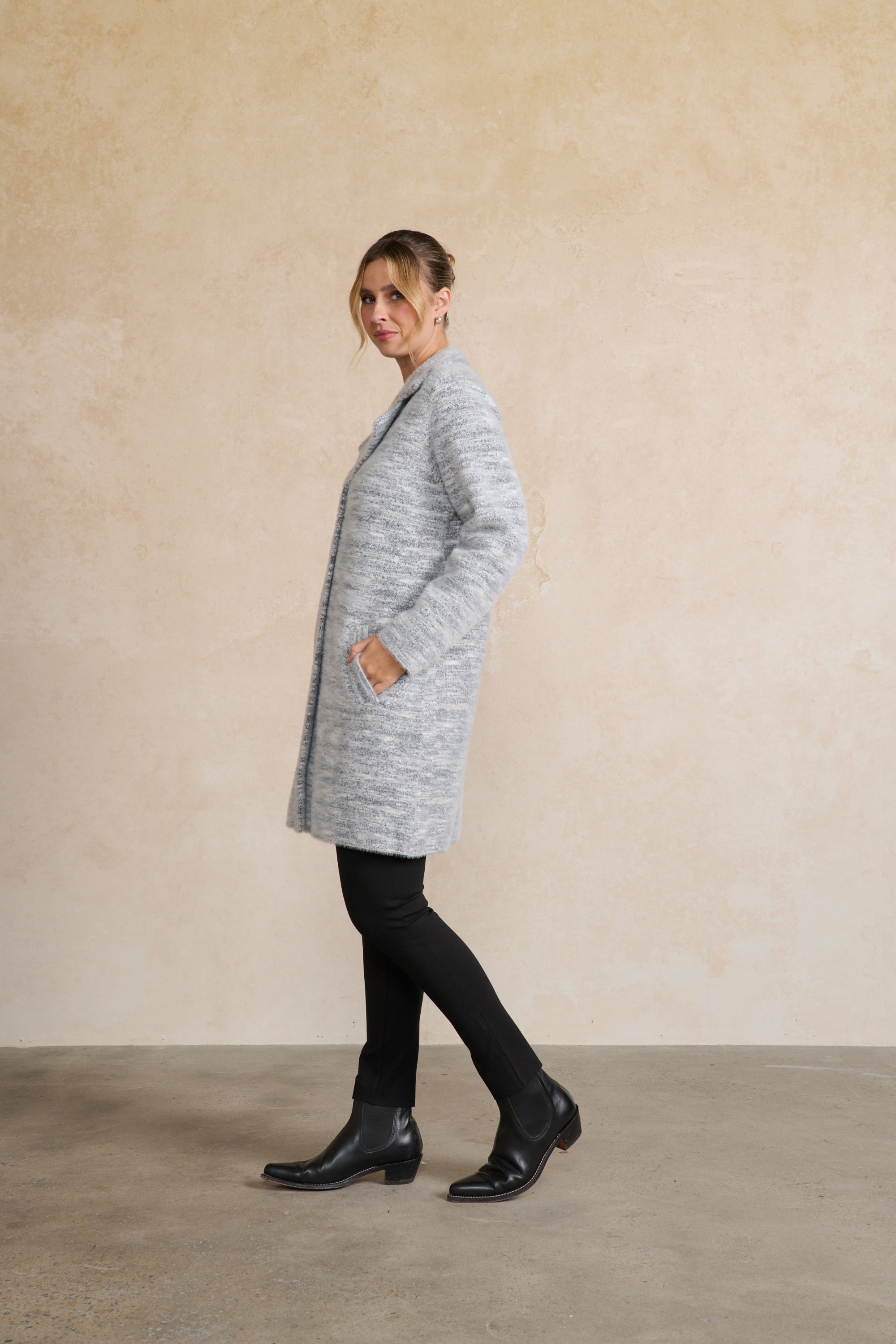 Woman wearing a gray coat standing against a beige wall.