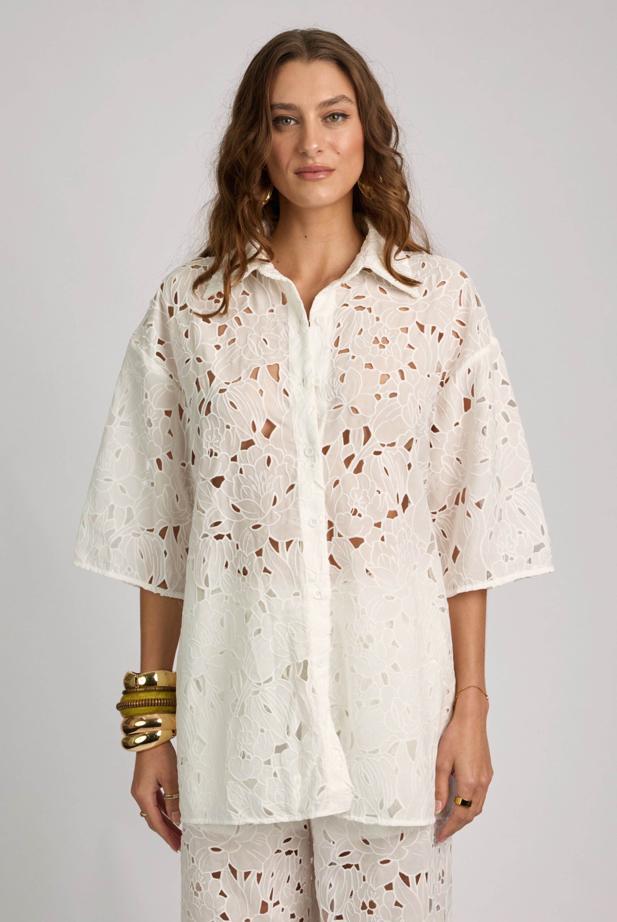 Woman wearing a white floral patterned shirt and pants on a gray background