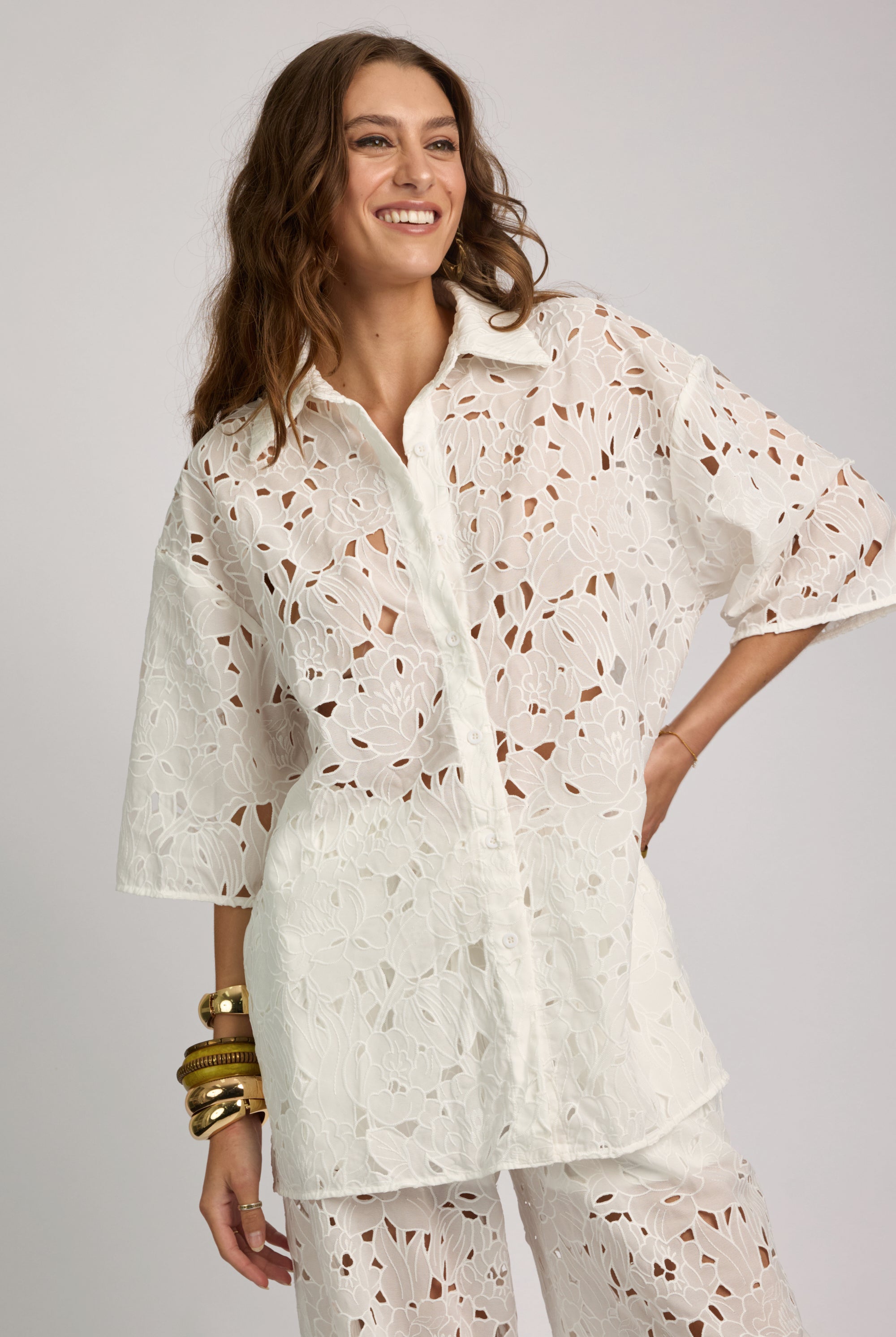 Woman wearing a white patterned shirt and pants on a gray background