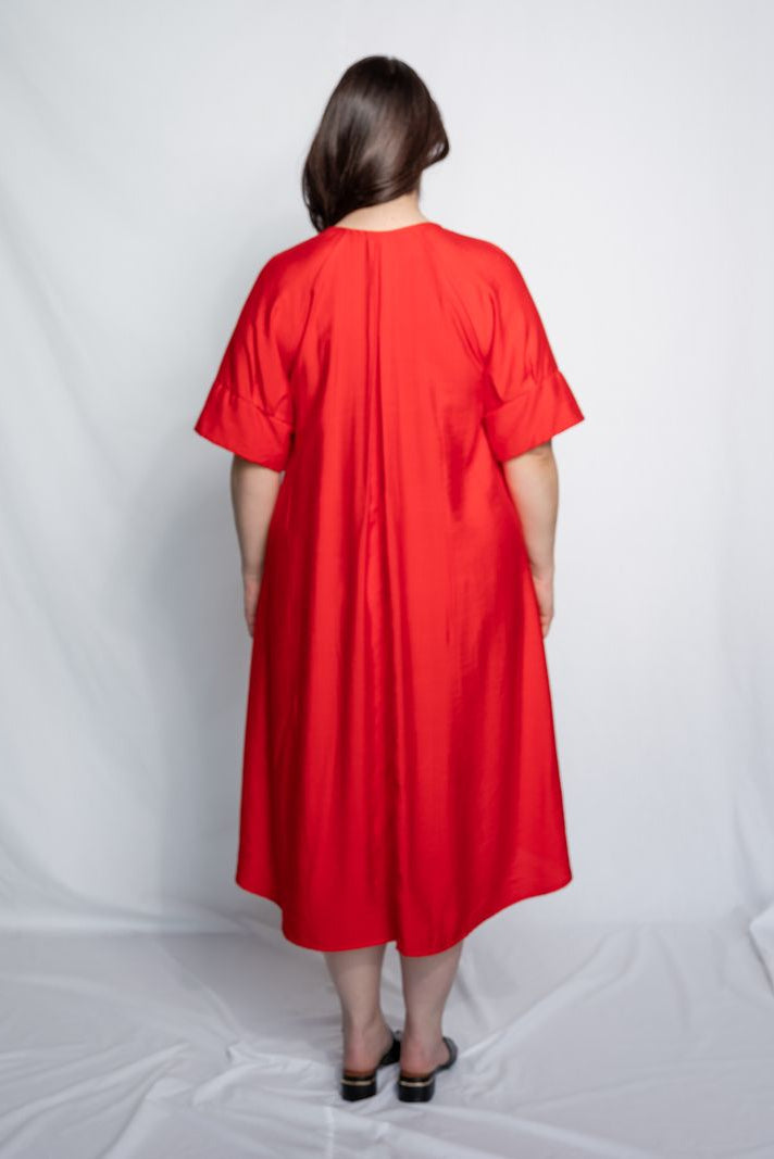 Woman wearing a v neck bright red midi length dress with elbow length sleeves and flower motif against a white background.