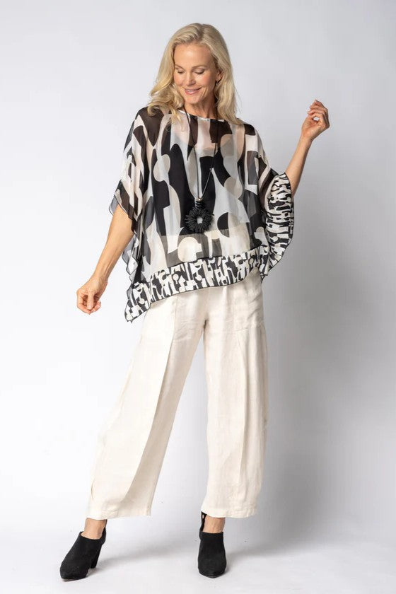 Woman wearing a black and white patterned top and white pants with a plain background