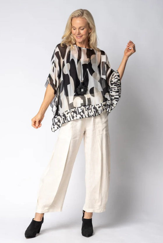 Woman wearing a black and white patterned top with white pants on a plain background