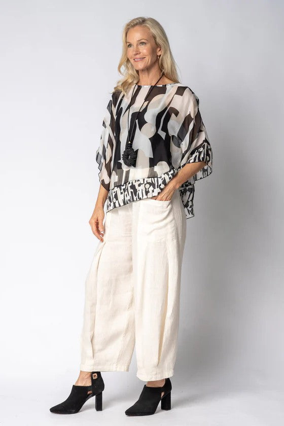 Woman wearing a black and white patterned top and white pants with a plain background