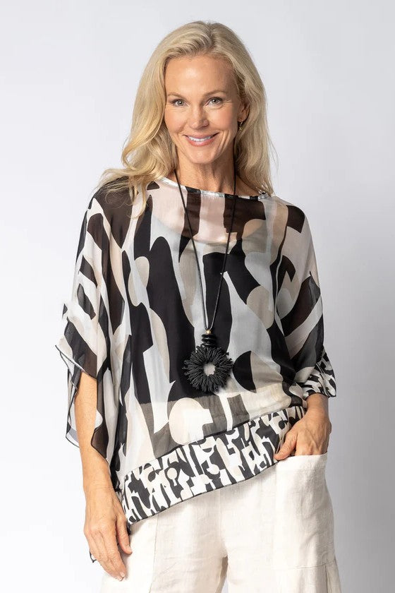 Woman wearing a black and white patterned top with a plain background