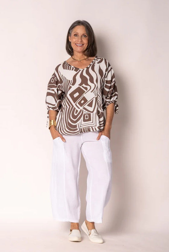 Woman wearing a patterned top and white pants against a plain background