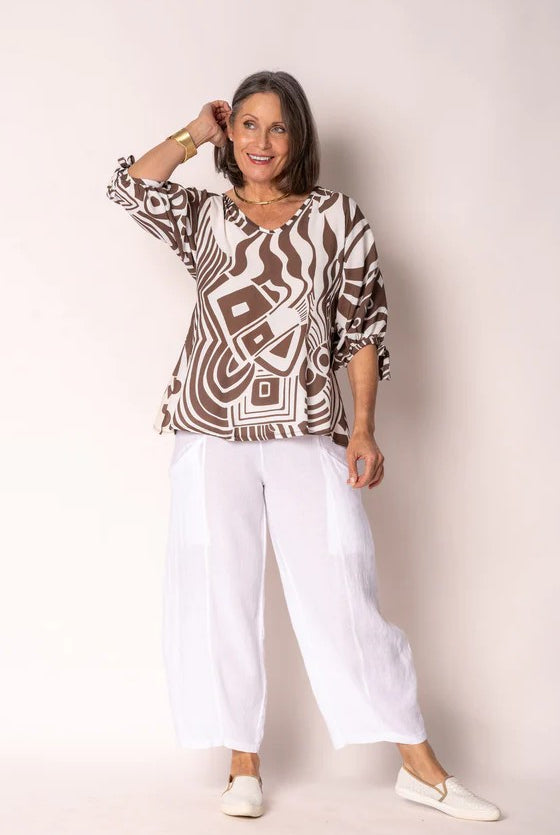 Woman wearing a patterned top and white pants against a plain background