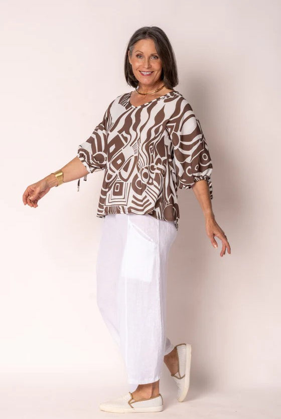 Woman wearing a patterned top and white pants on a plain background