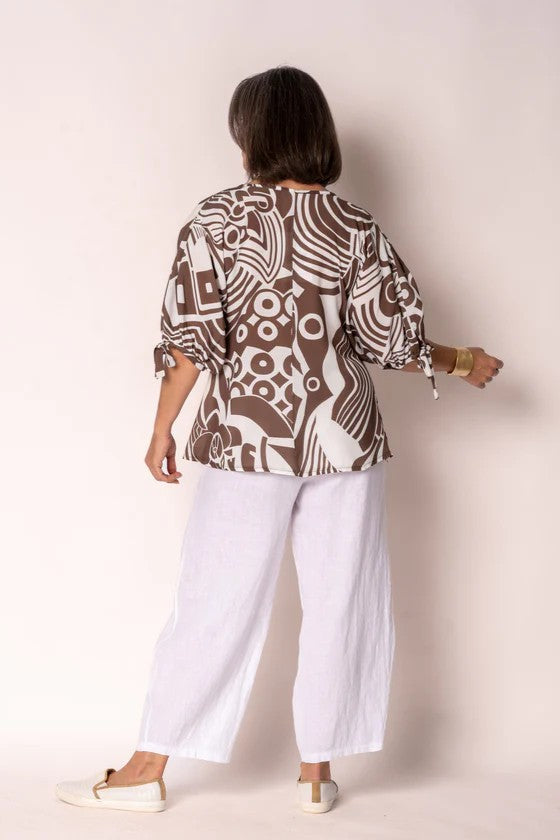 Person wearing a patterned top and white pants against a plain background
