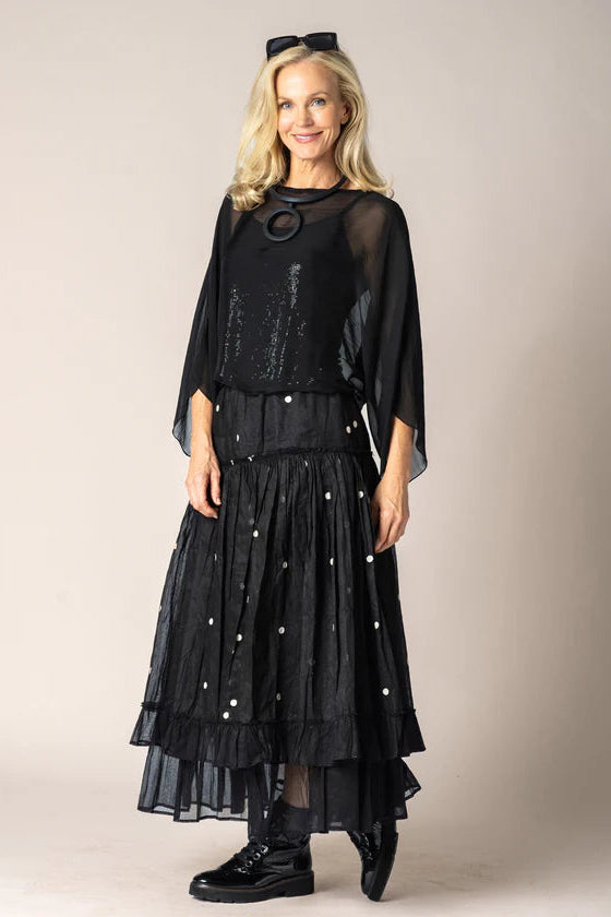 Woman wearing a black outfit with sheer sleeves and a long skirt against a beige background