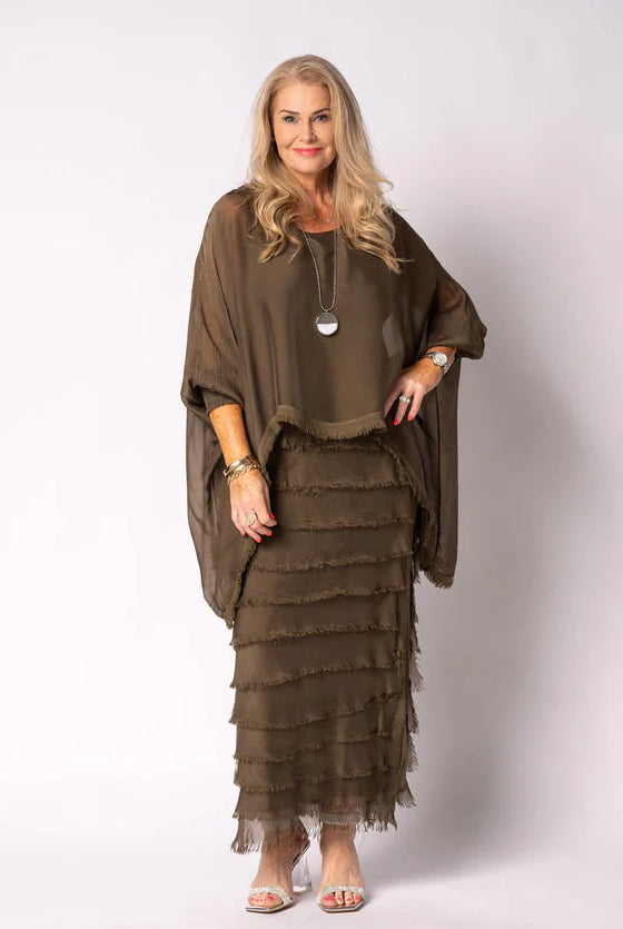 Woman wearing a moss green layered dress and poncho against a white background