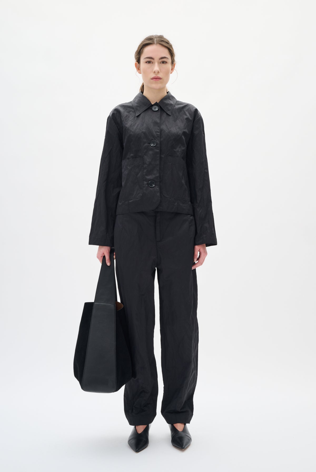 Person wearing a black outfit holding a black bag on a white background