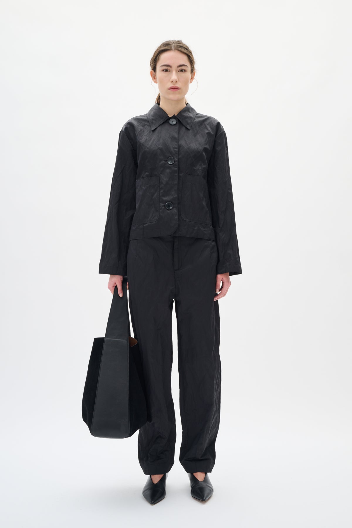 Person wearing a black outfit holding a black bag on a white background
