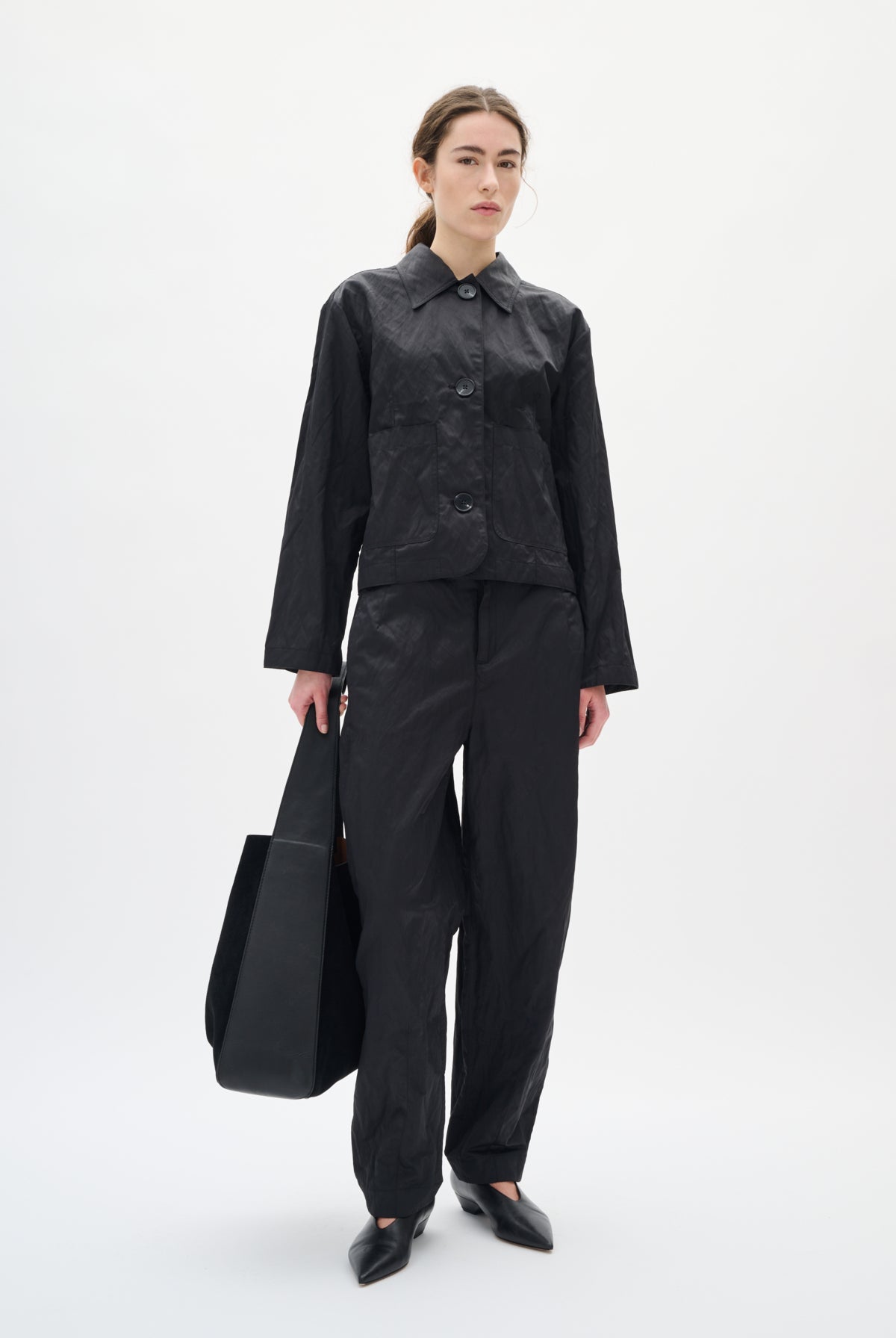 Person wearing a black outfit holding a black bag on a white background