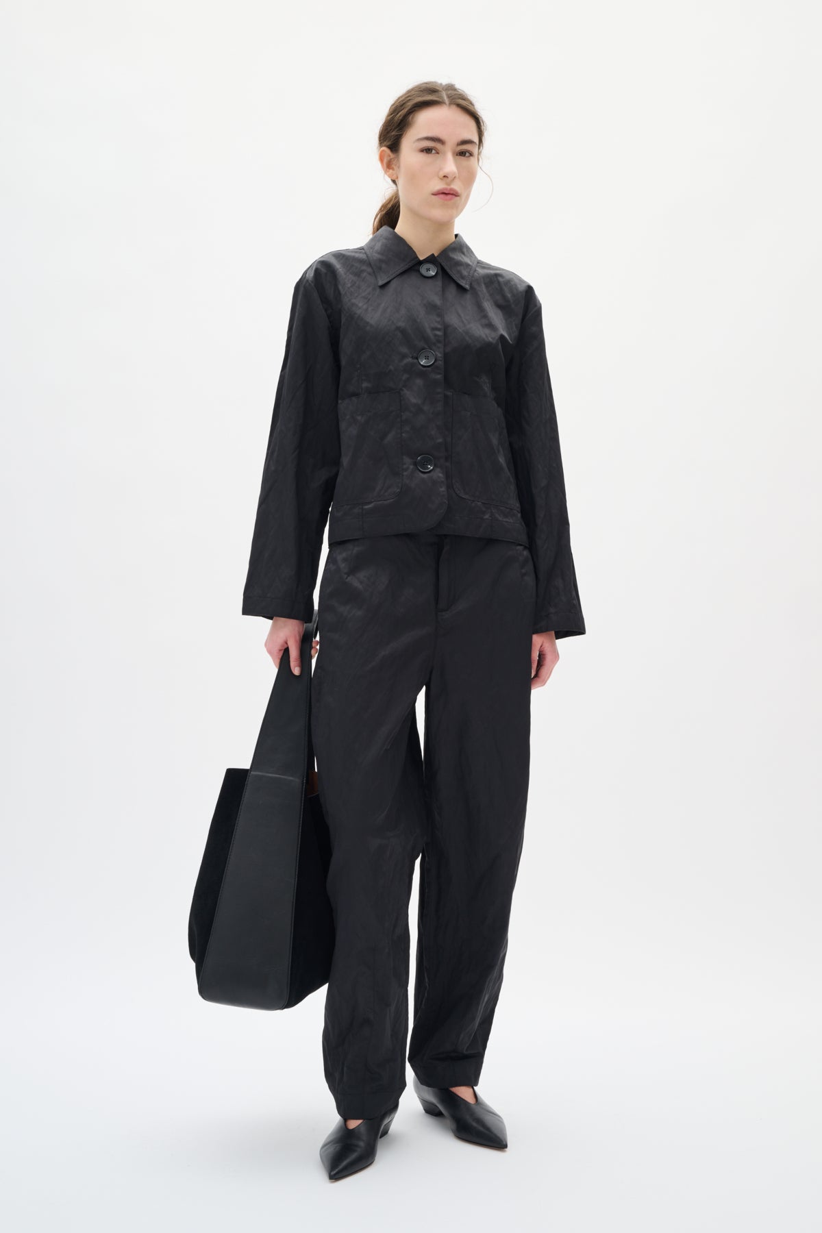 Person wearing a black outfit holding a black bag on a white background