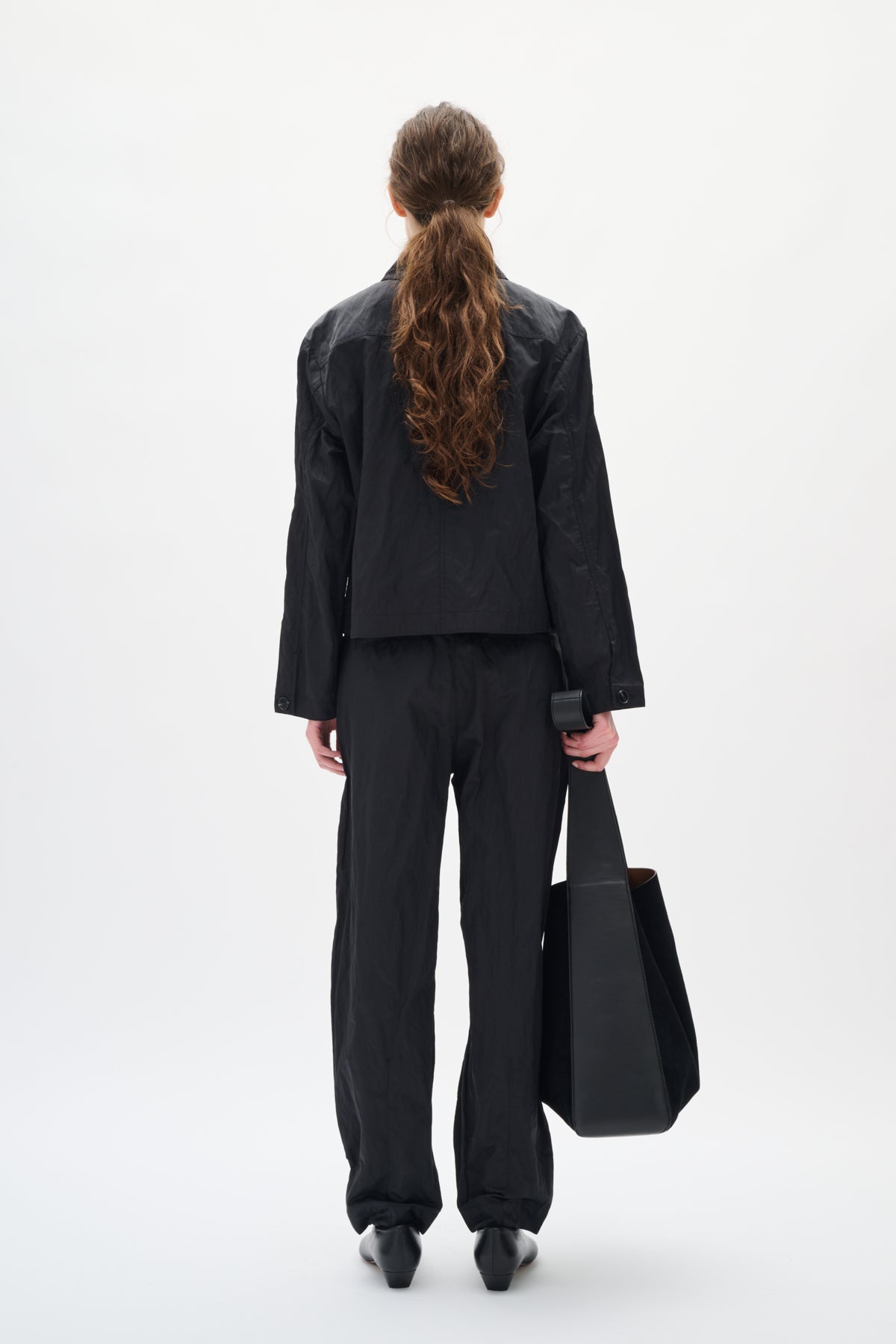 Person wearing a black suit holding a black bag on a white background back angle