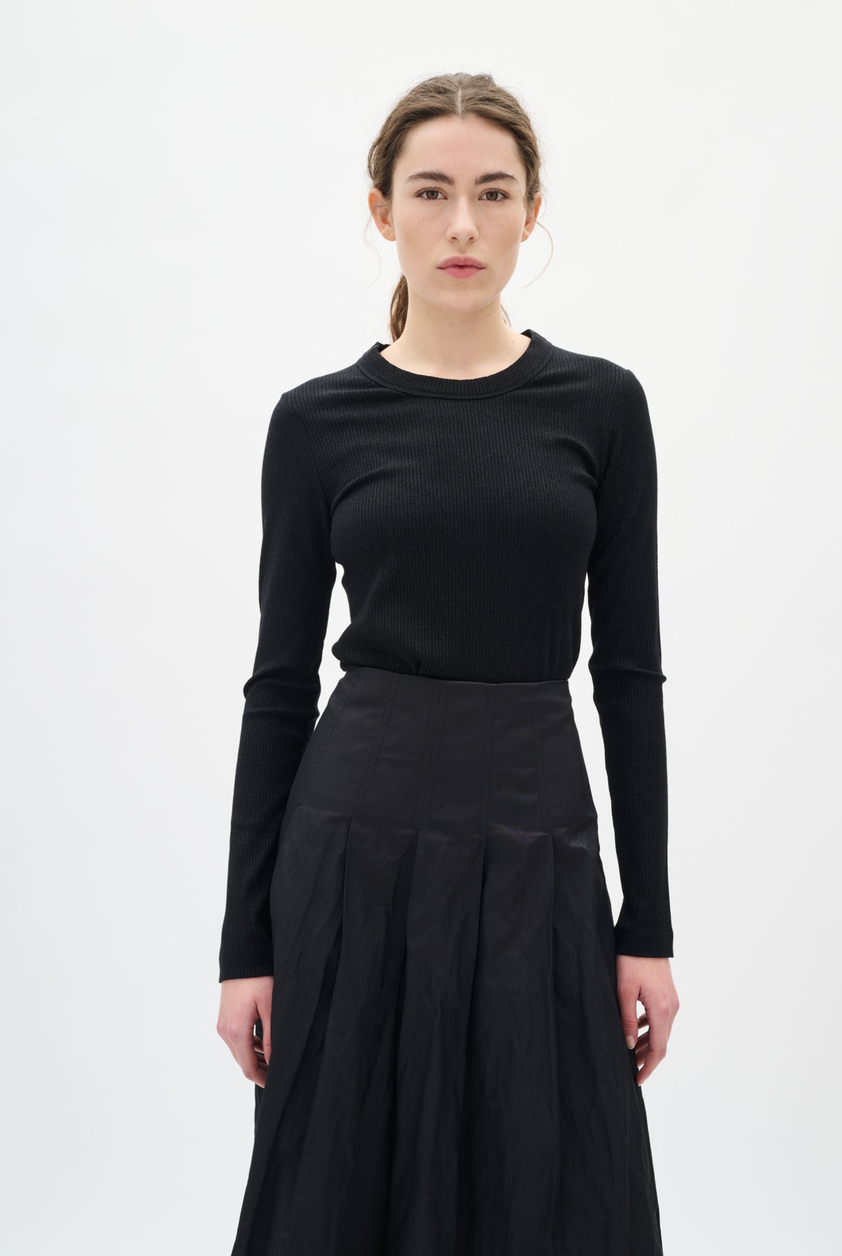 Woman wearing a black long-sleeve top and black skirt on a white background