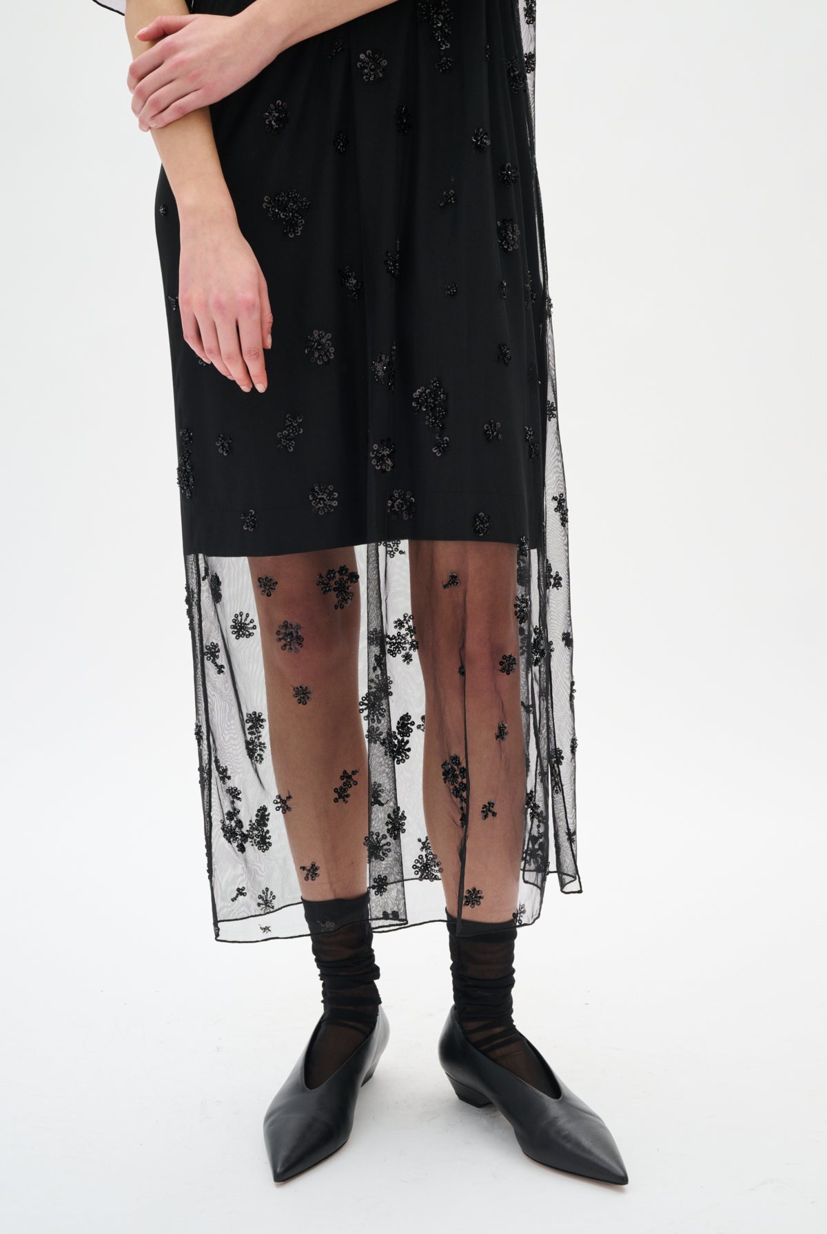 Black dress with floral embroidery, sheer overlay, black tights, and black shoes on a white background
