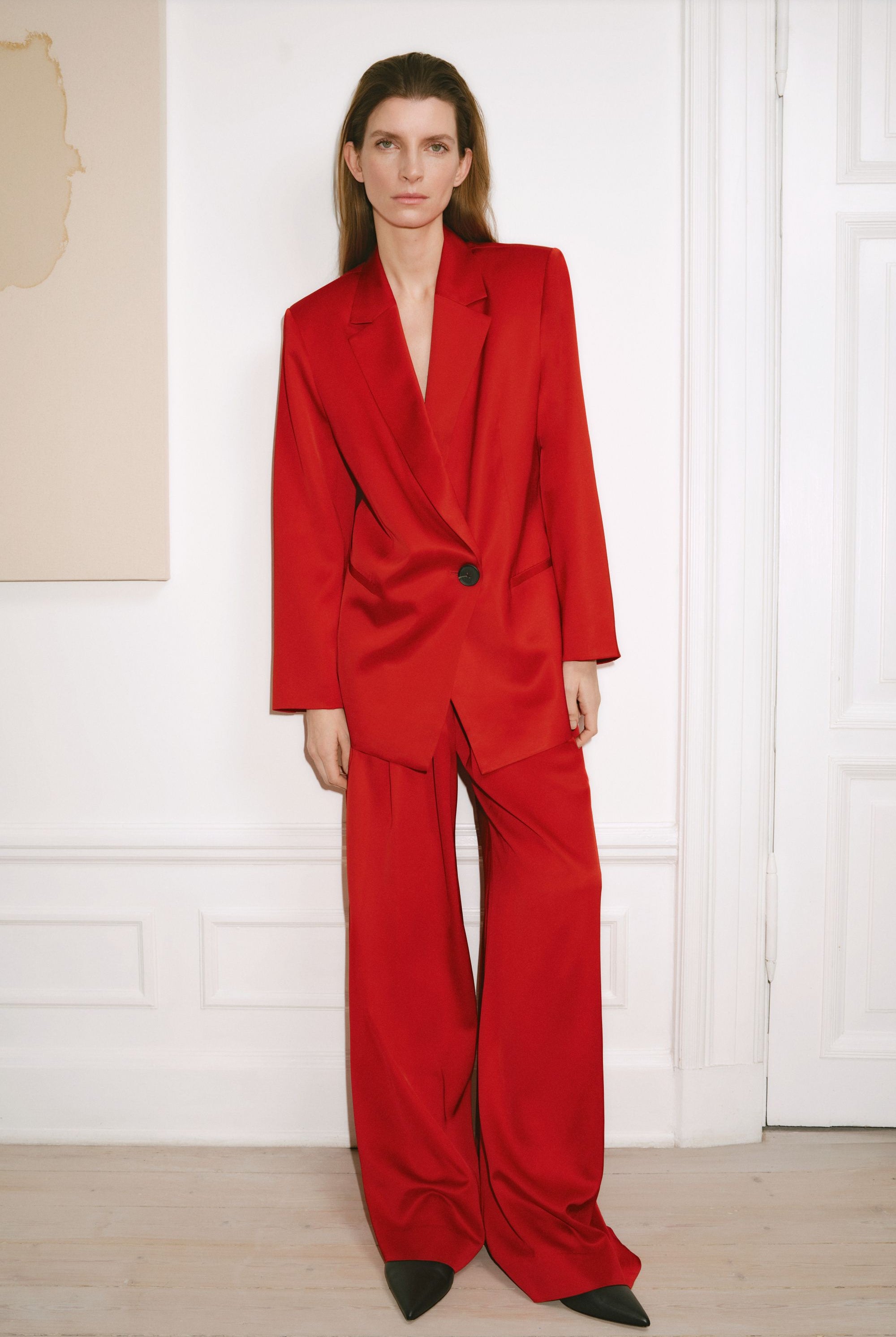 Woman wearing a red suit standing against a white wall.