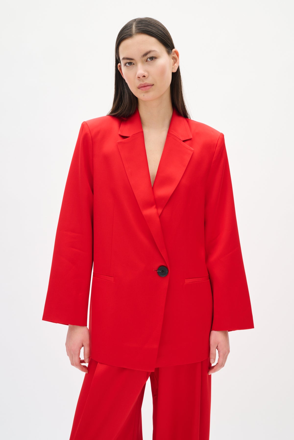 Woman wearing a red suit with a black button on a white background