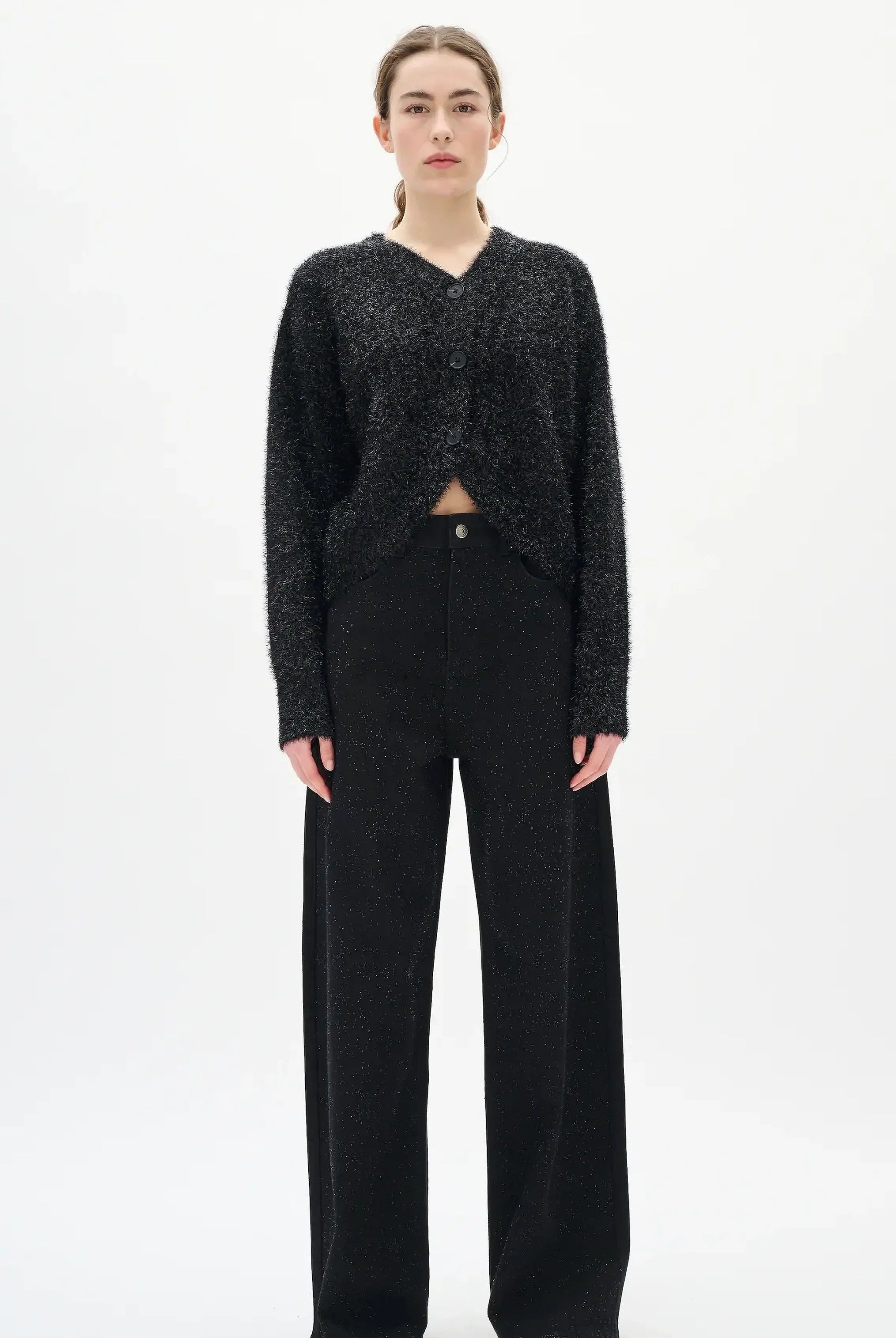 Woman wearing a black textured sweater and diamante black jeans on a white background