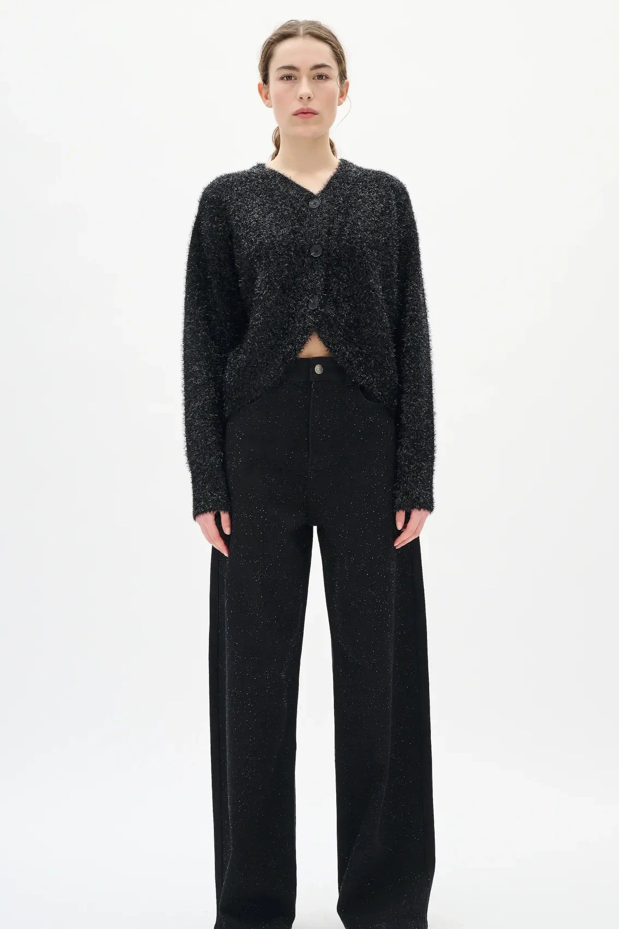 Woman wearing a black textured sweater and diamante black jeans on a white background