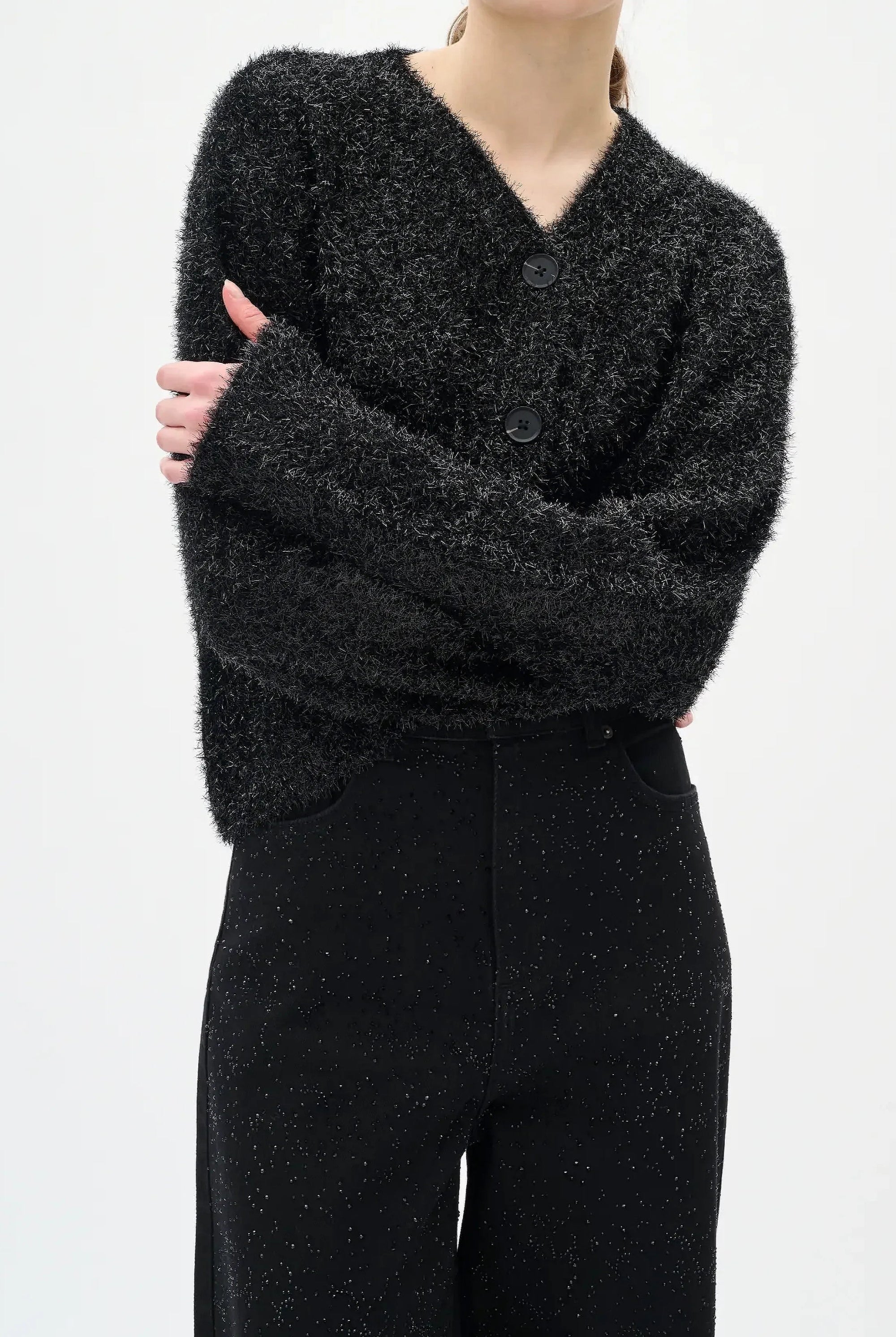 Woman wearing a black textured sweater and diamante black jeans on a white background