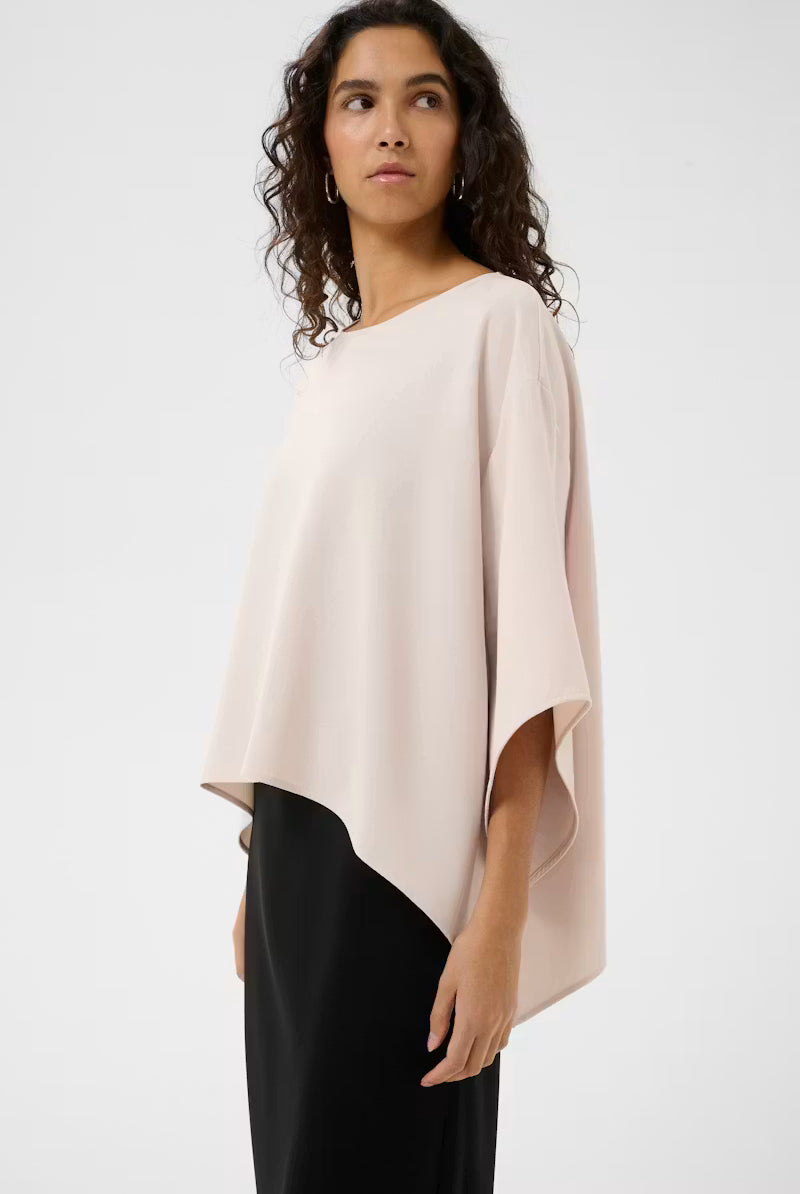 Woman wearing a beige poncho over a black outfit on a white background