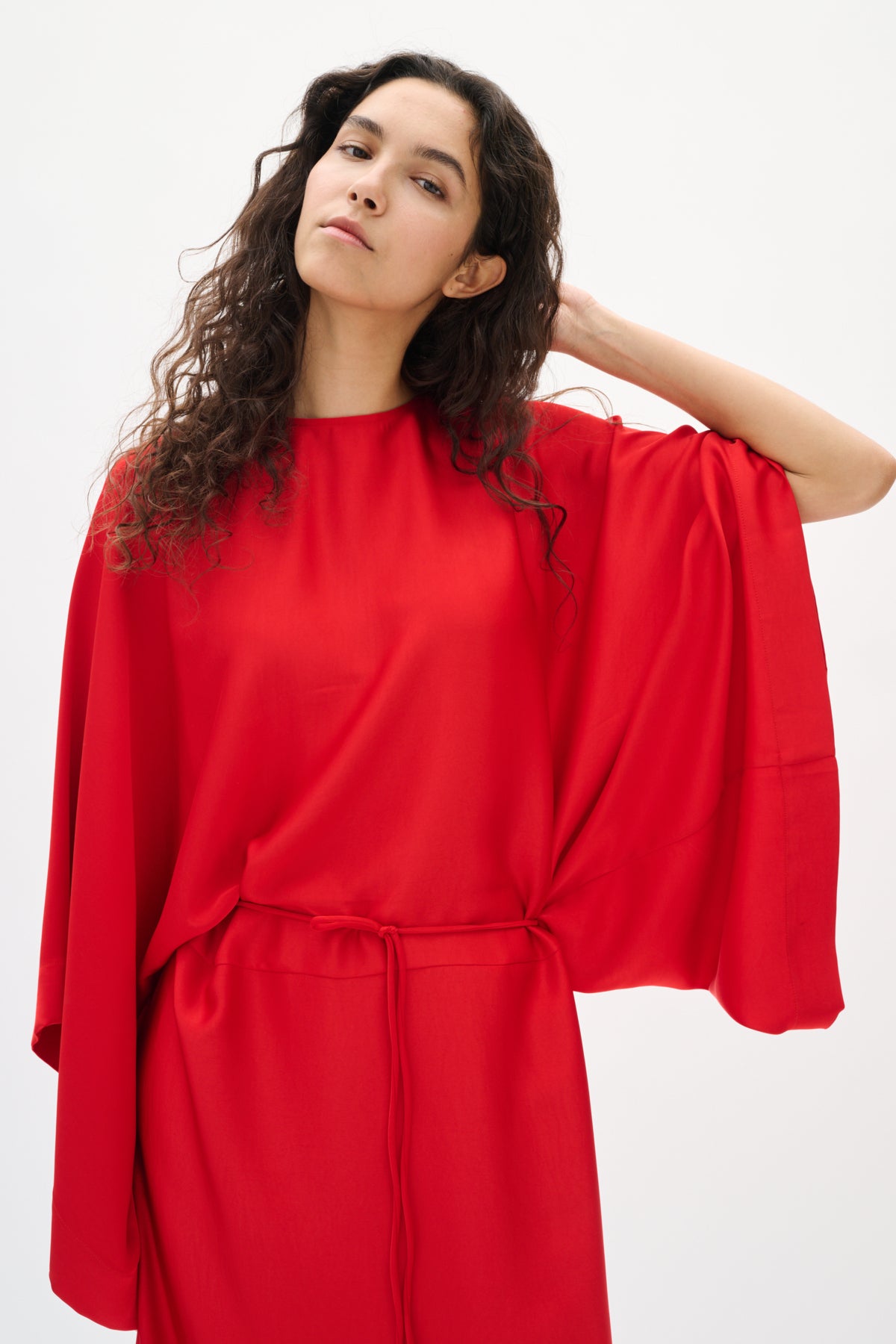 Woman wearing a red dress with wide sleeves on a white background