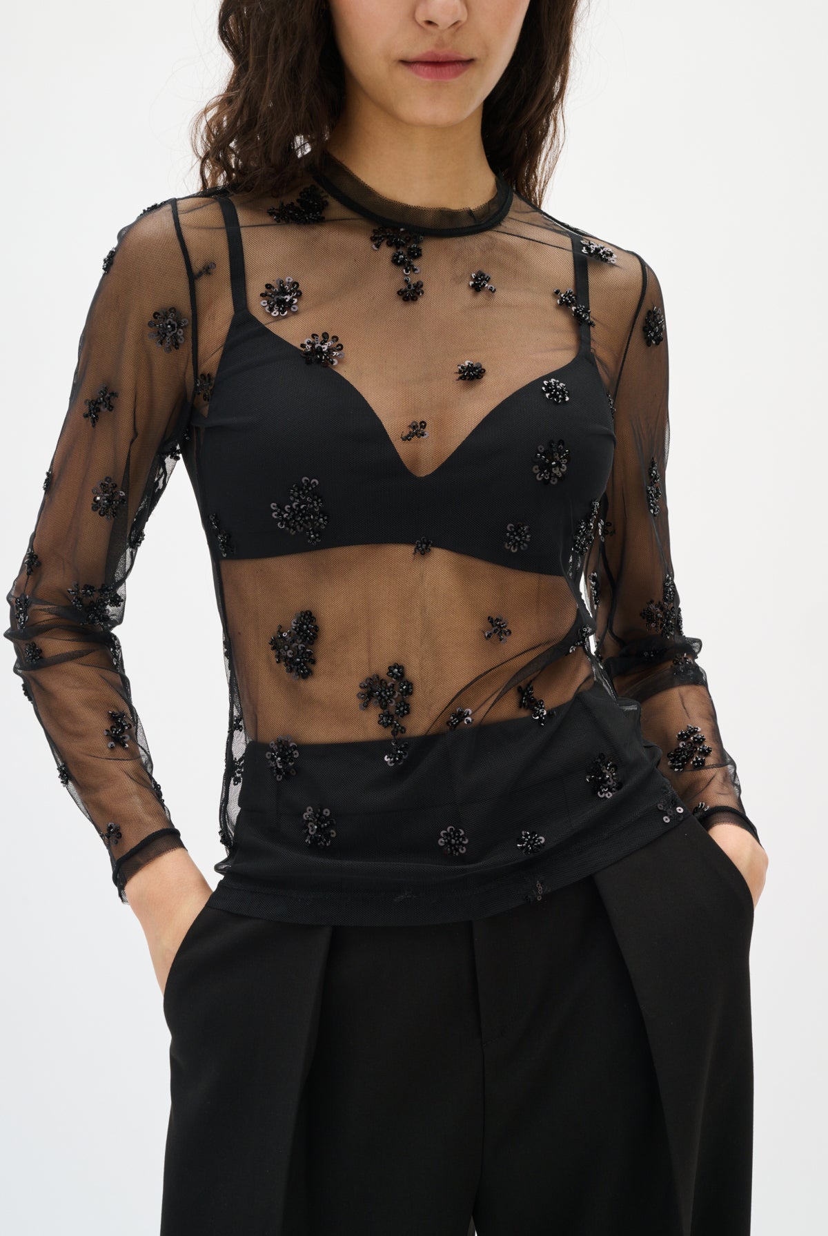 Black sheer top with floral embellishments worn by a model on a white background