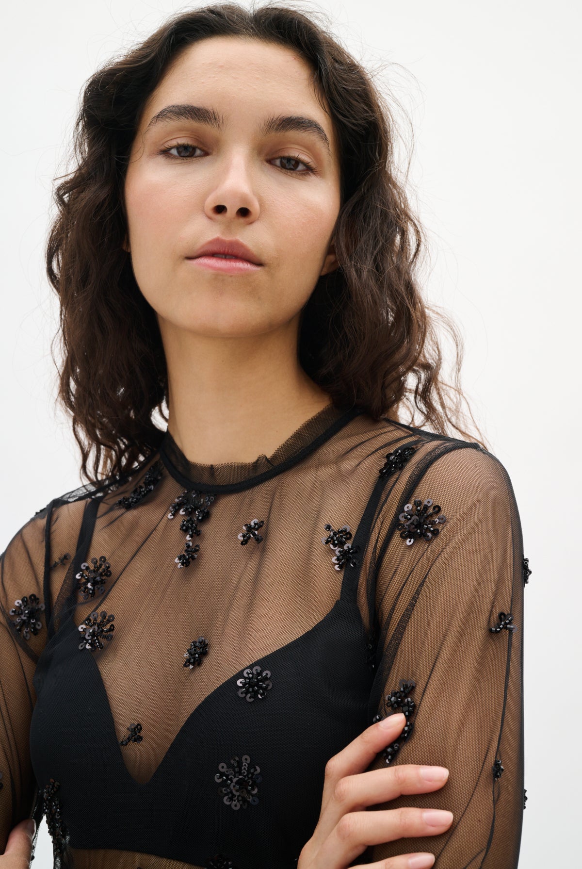 Woman wearing a black sheer top with floral embellishments on a white background