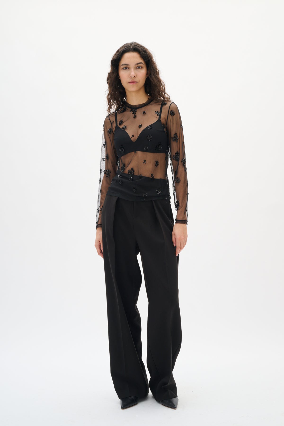 Woman wearing a black sheer top with floral patterns and black pants on a white background