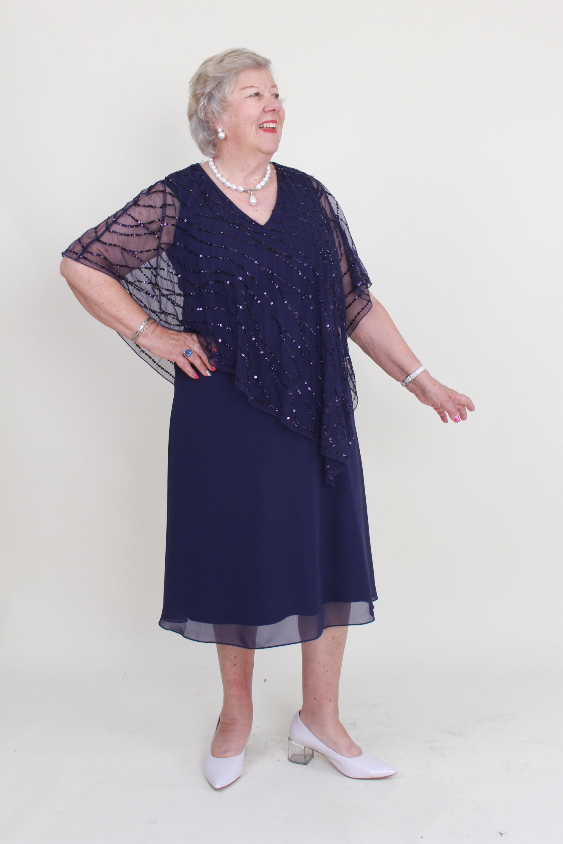 Person wearing a navy blue beaded dress with sheer sleeves on a white background