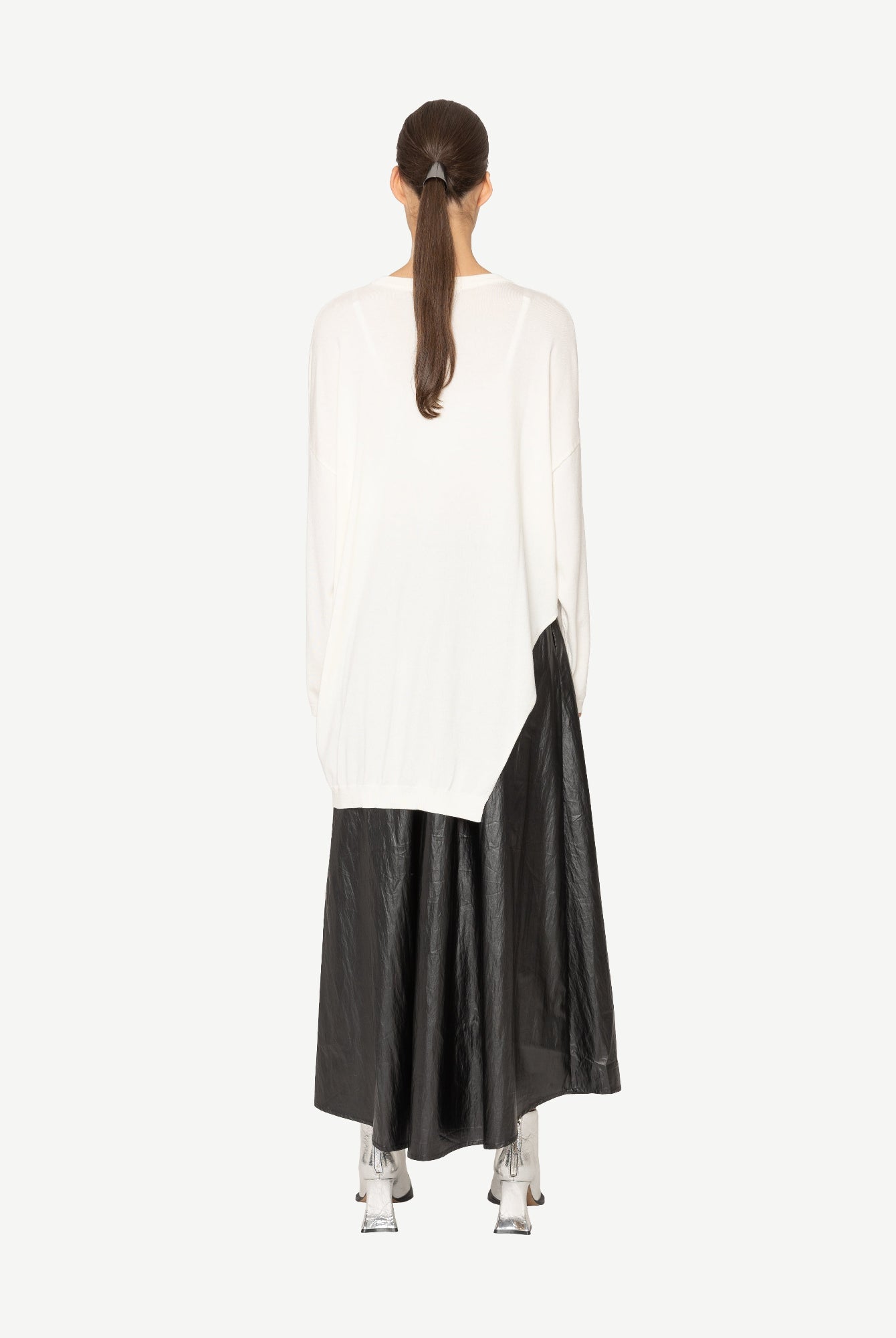 Woman wearing a white top with branch print and a long black skirt on a white background back angle