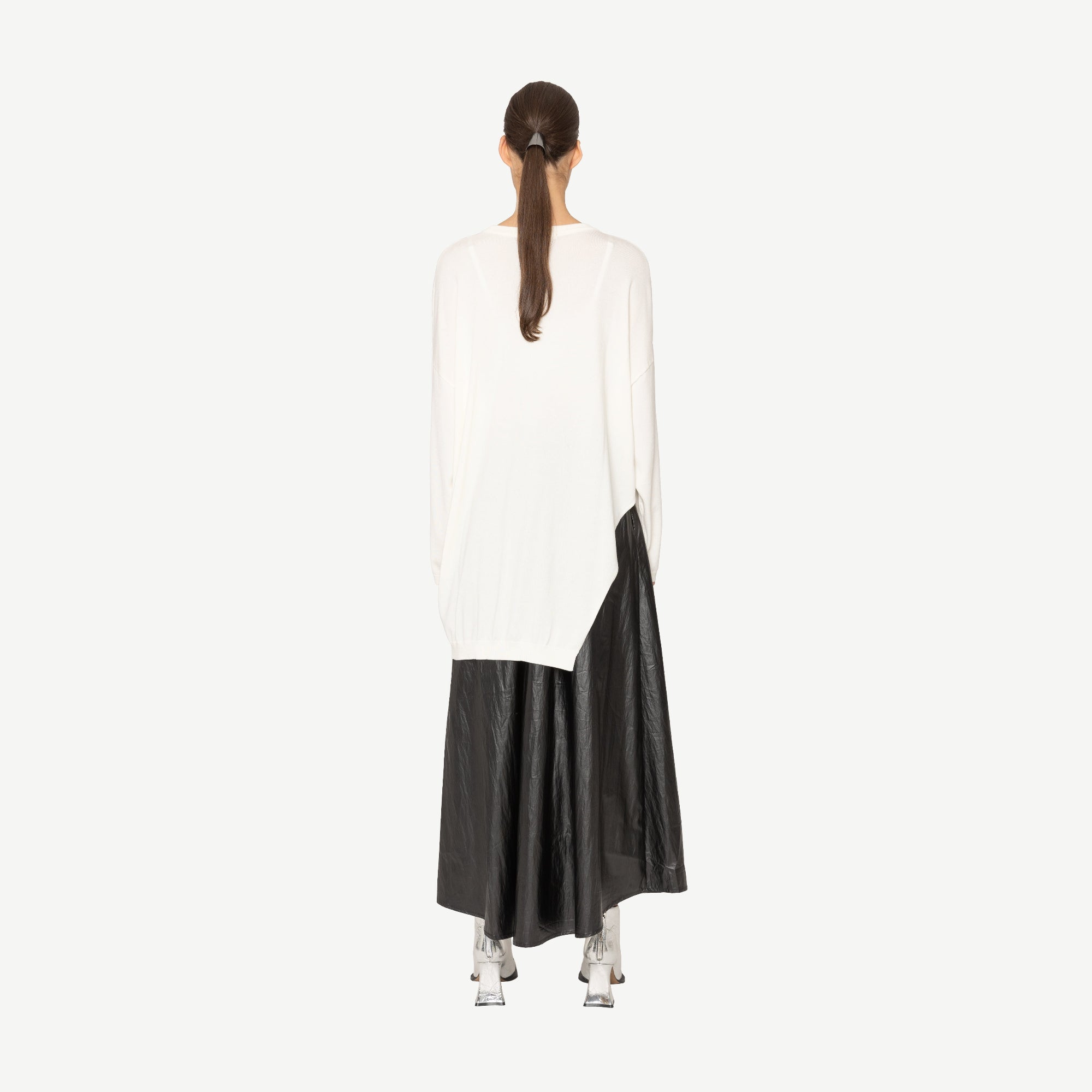 Woman wearing a white top with branch print and a long black skirt on a white background back angle