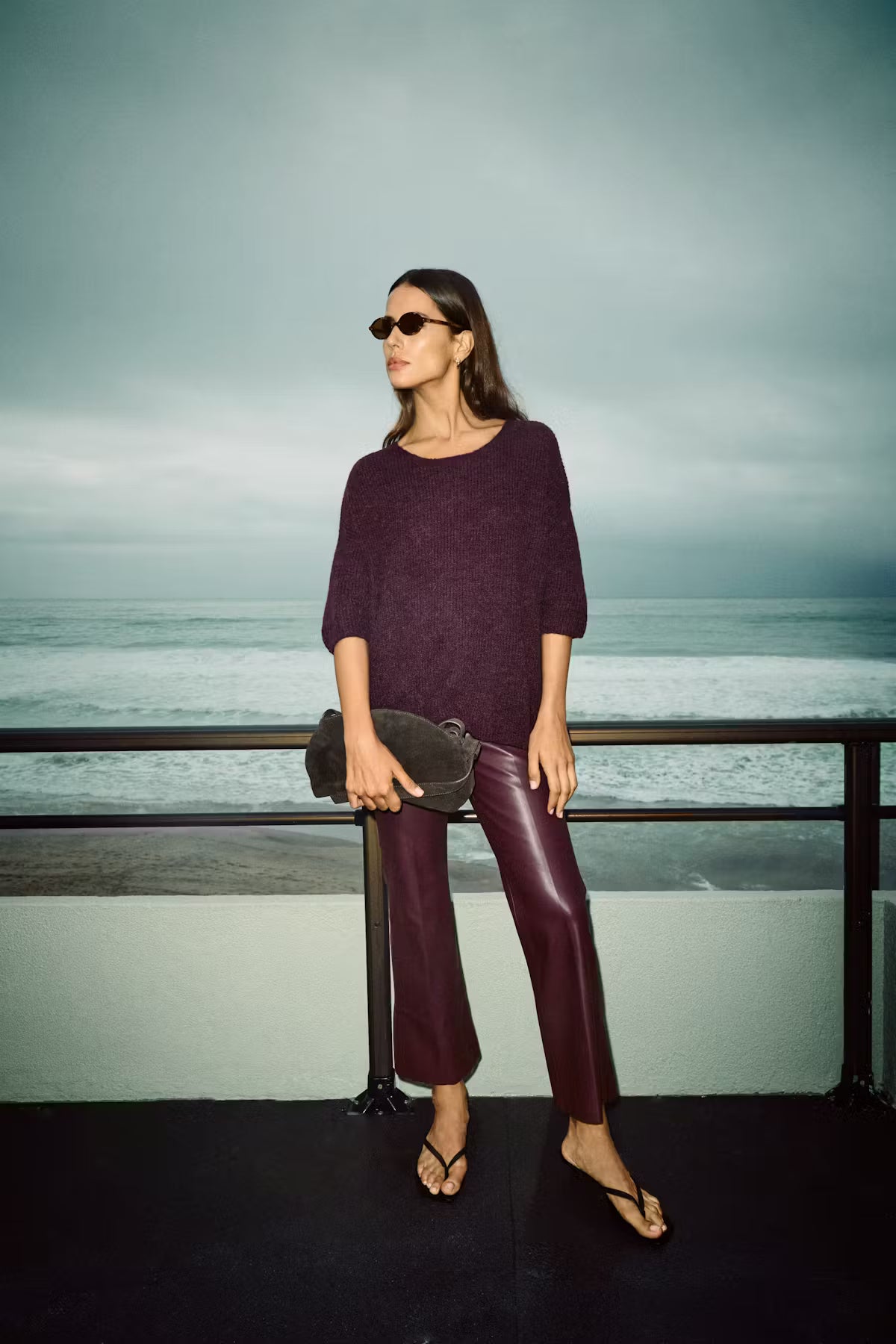 Woman in a purple sweater and red pants standing on a balcony with a scenic background