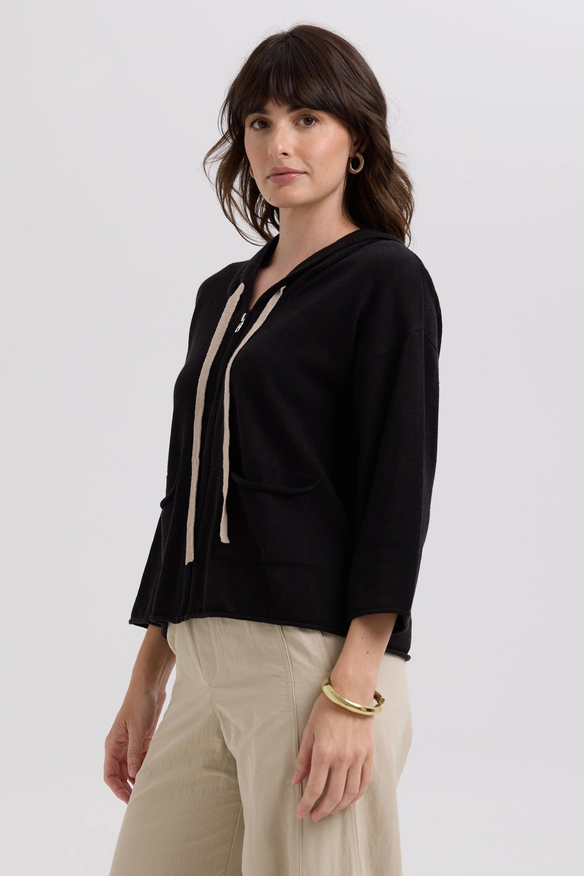 Woman wearing a black top with a beige ribbon and beige pants on a white background