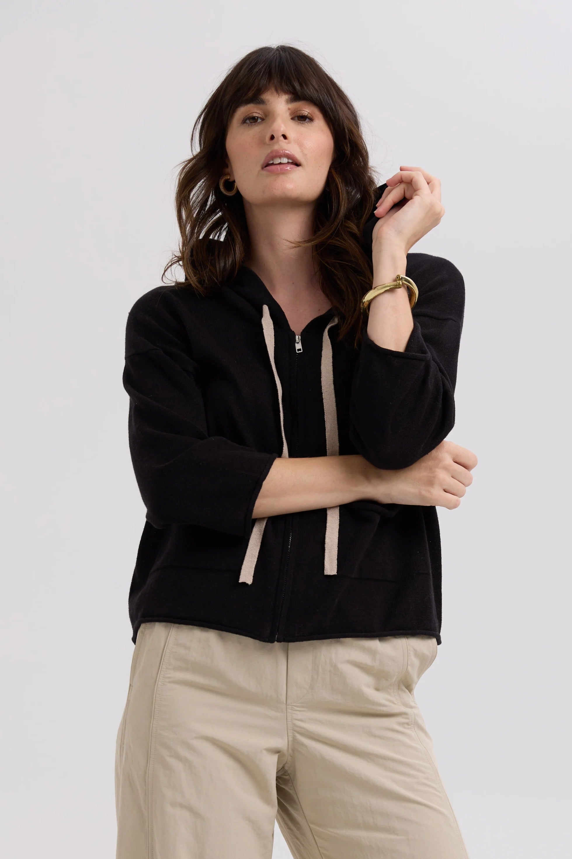 Woman wearing a black hoodie with beige accents on a plain background