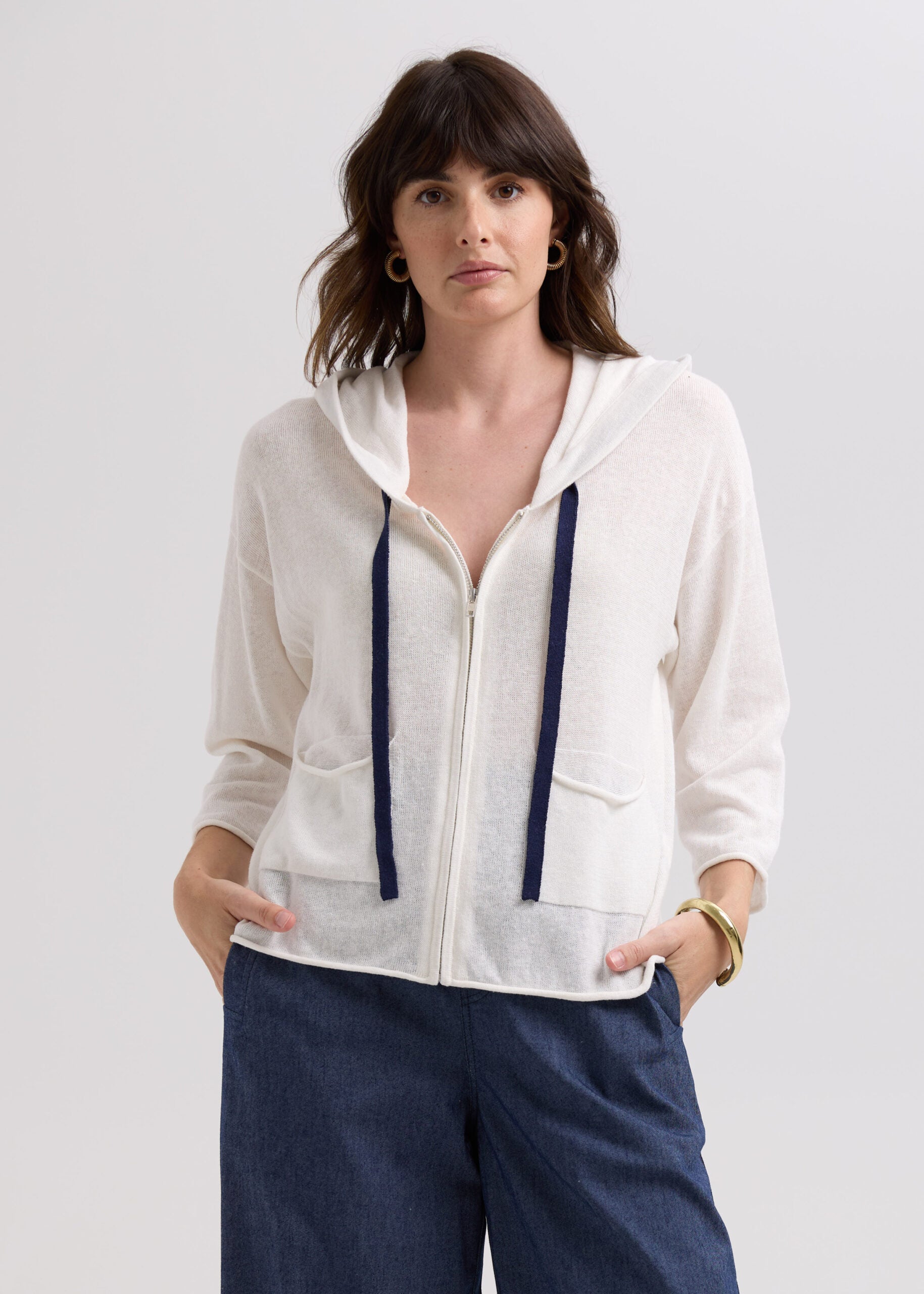 Woman wearing a white zip-up hoodie with navy drawstrings on a light gray background