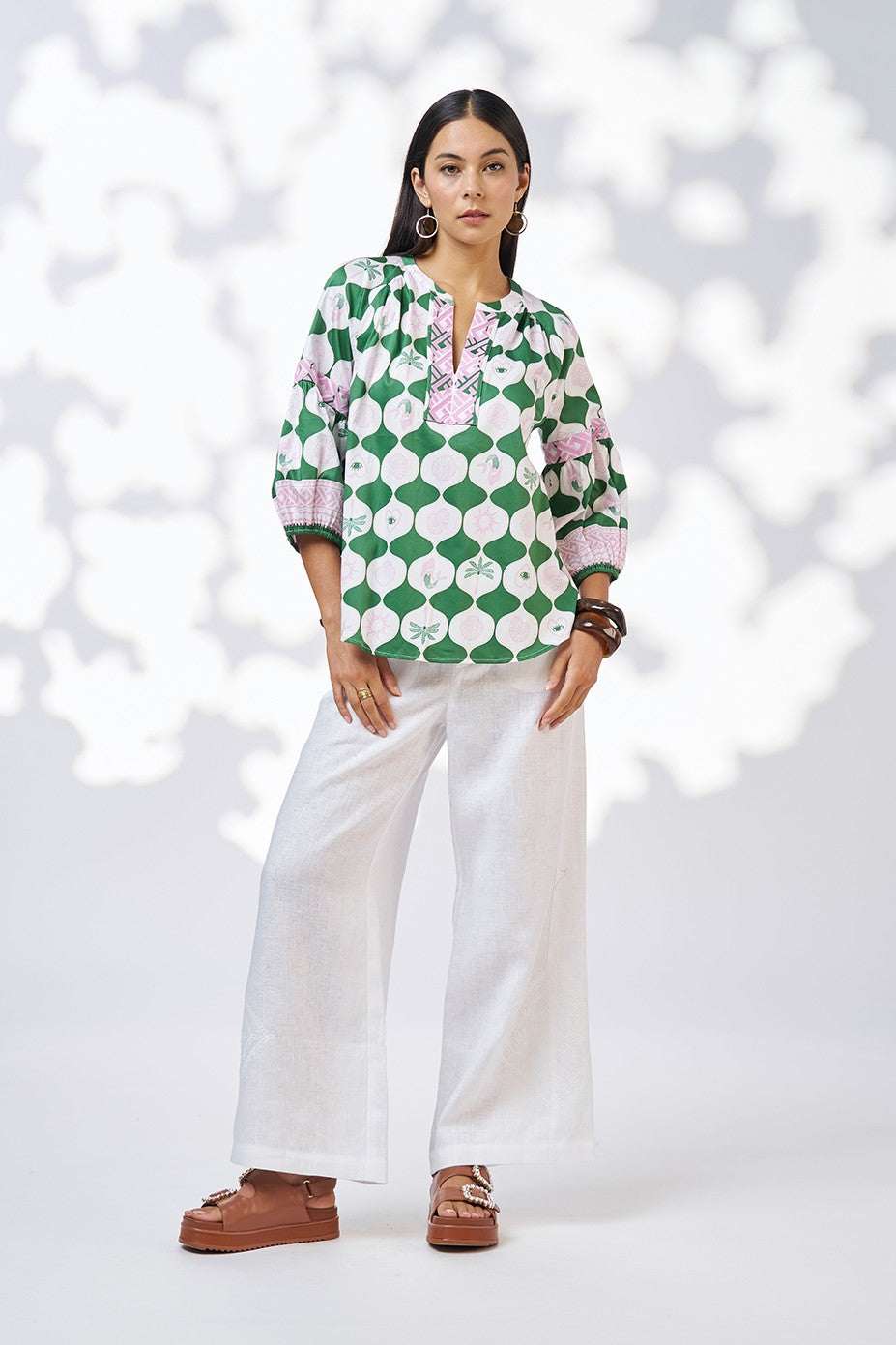model wearing green white and pink patterned blouse and white pant