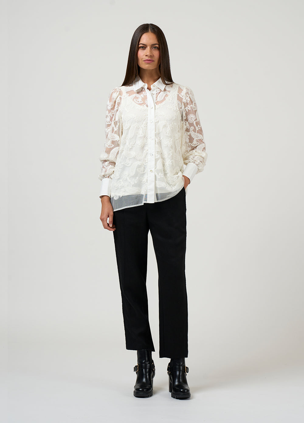 Woman wearing a white lace blouse and black pants on a white background