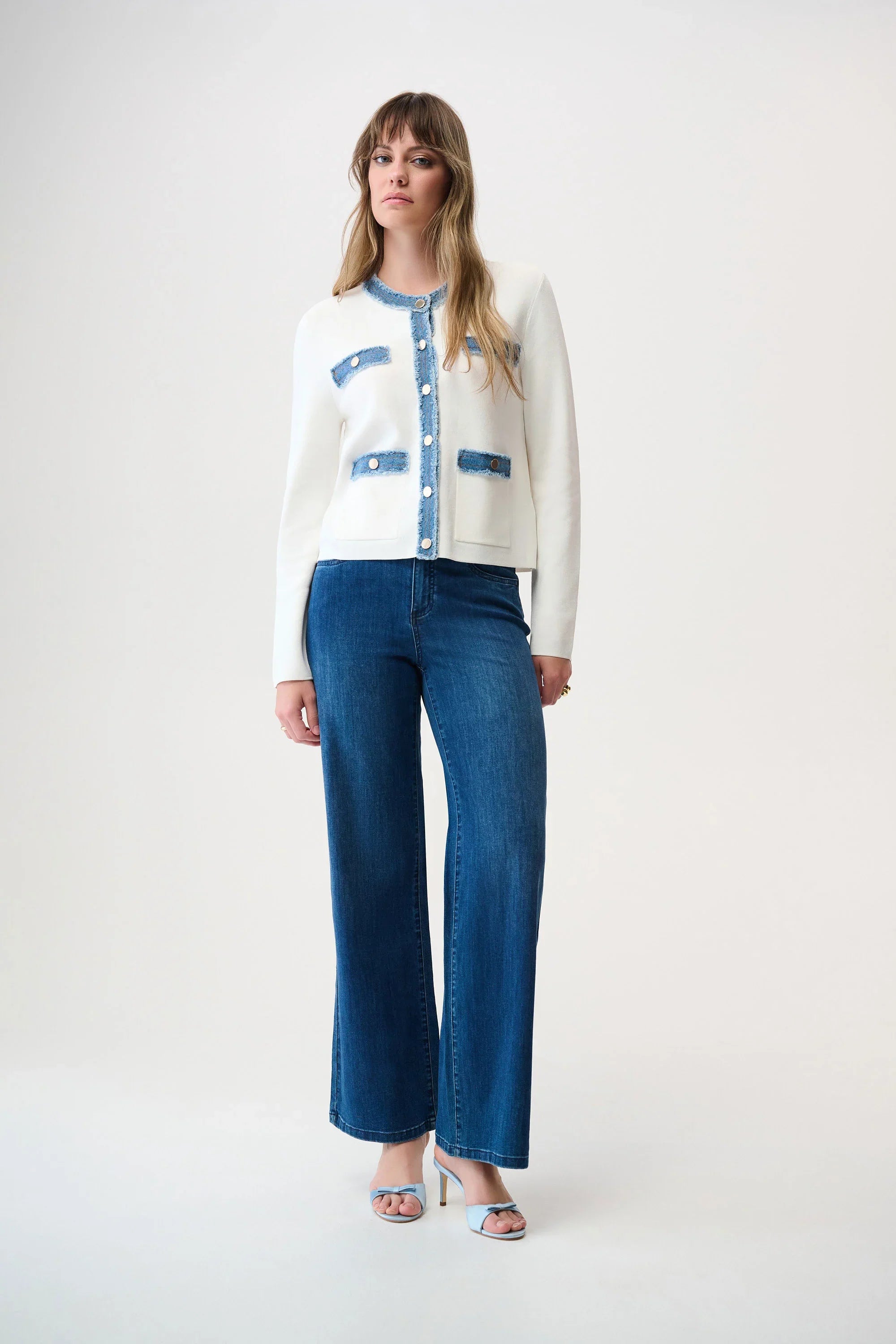 Woman wearing a white cardigan with blue accents and blue jeans on a white background