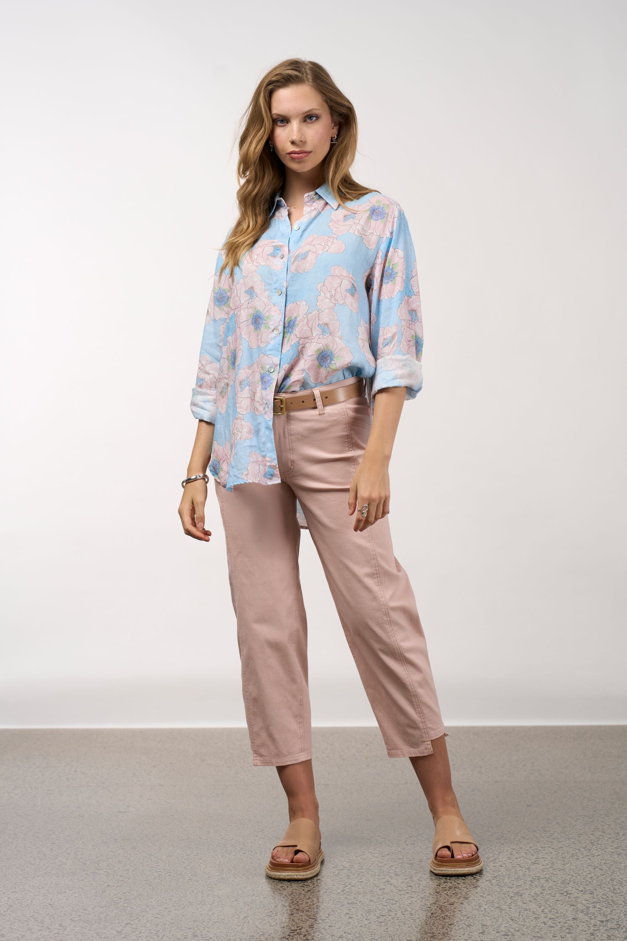 Woman wearing a light blue floral blouse and pink pants against a white background