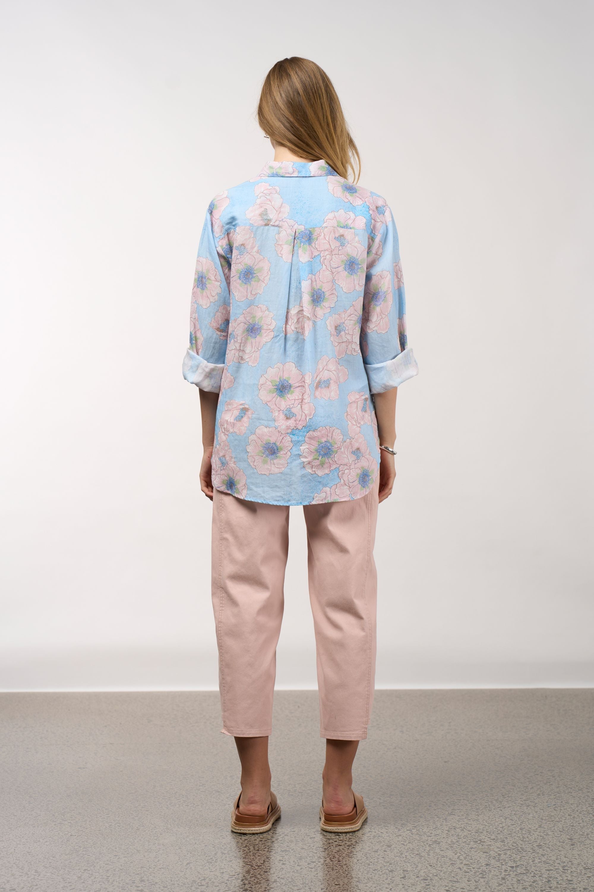 Person wearing a light blue floral blouse and pink pants on a white background