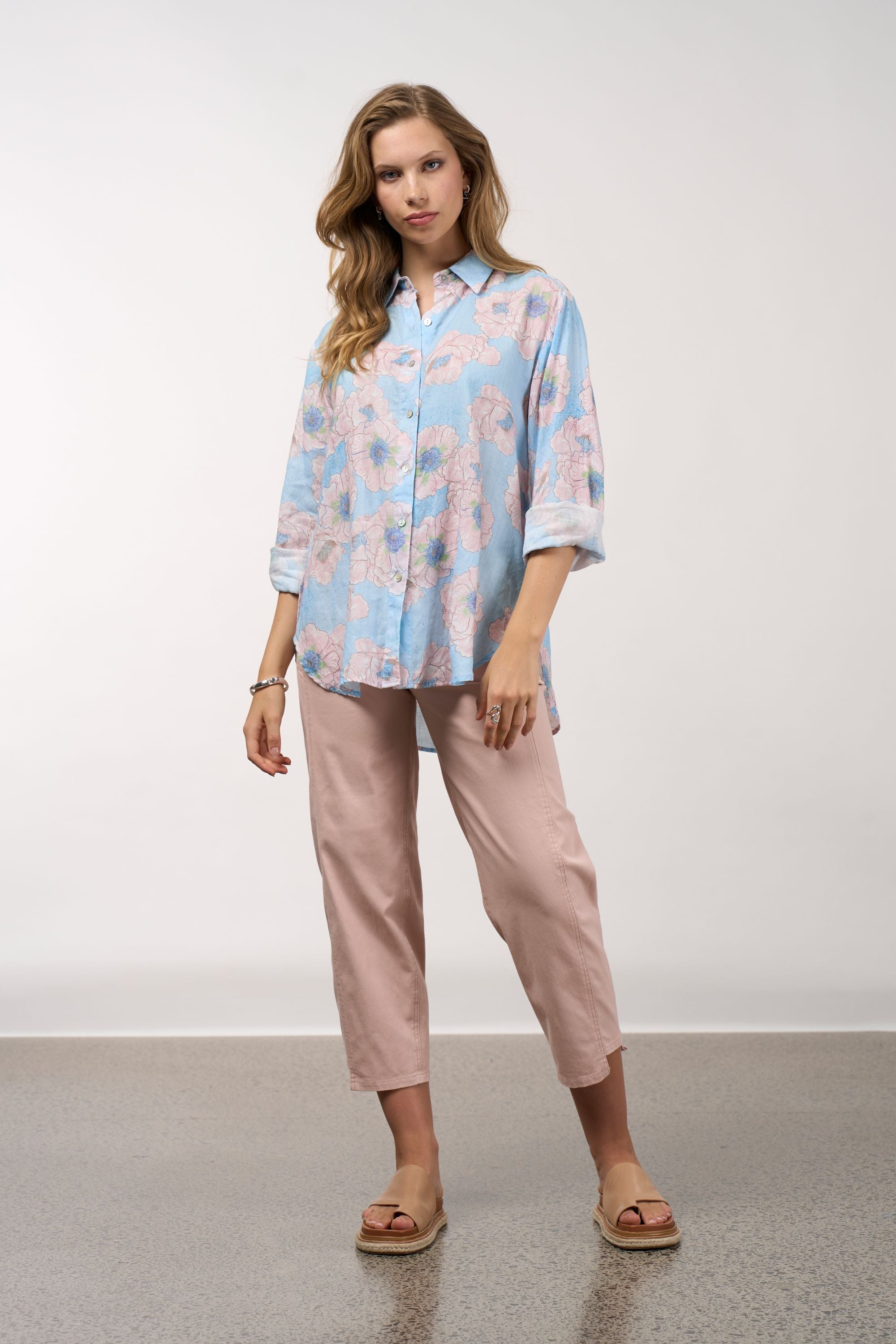 Woman wearing a light blue floral blouse and pink pants against a white background