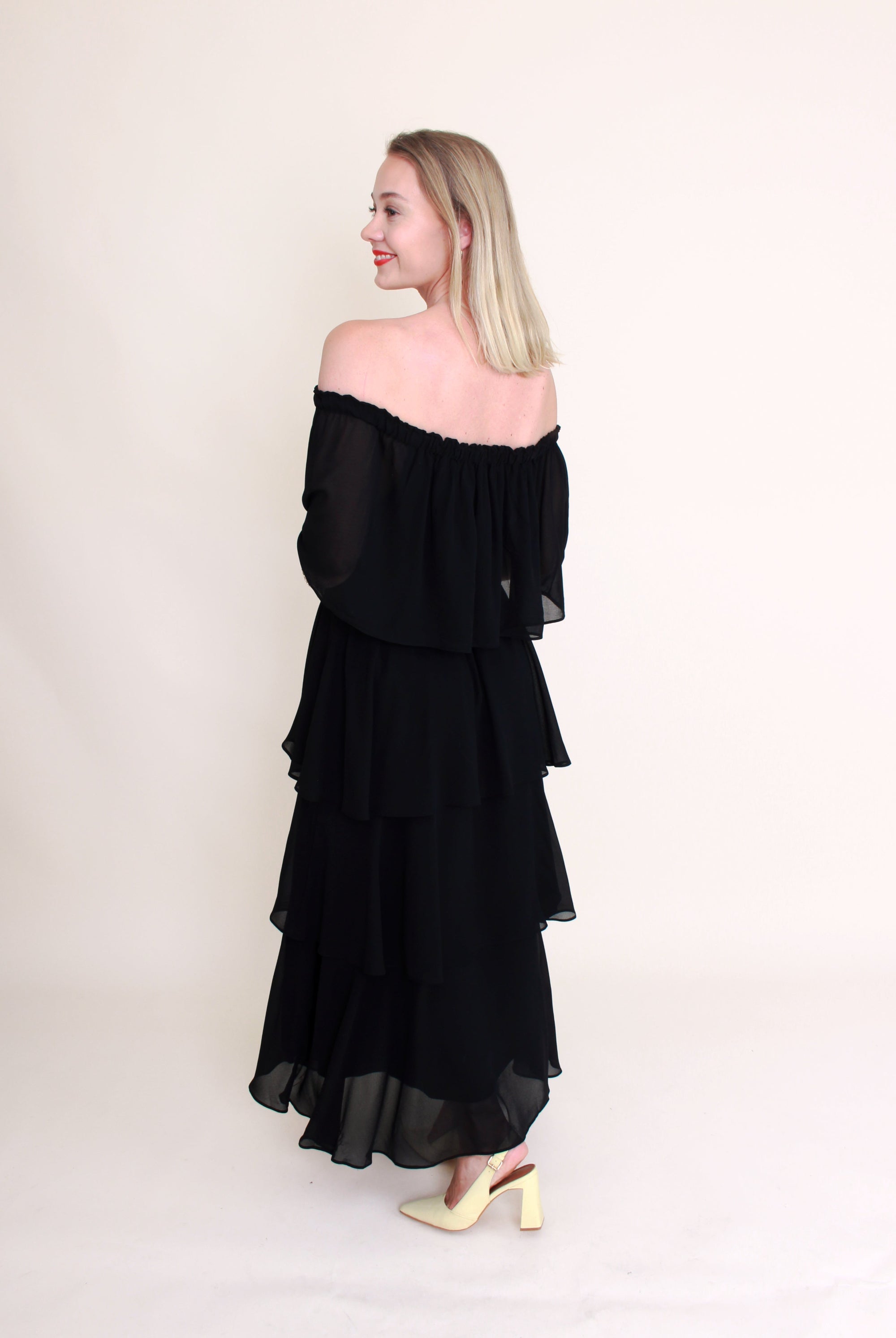 woman wearing off the shoulder black dress back view plain background