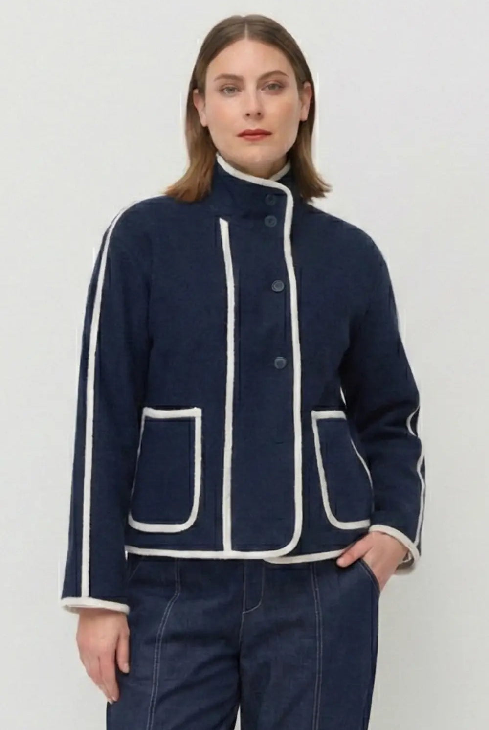 Person wearing a navy blue jacket with white trim on a plain background