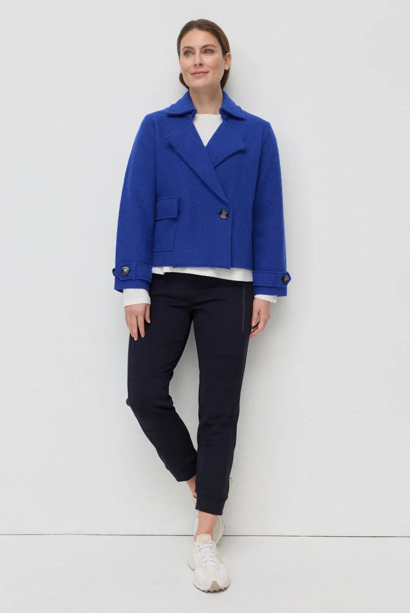Woman wearing a blue coat, white shirt, and black pants on a white background