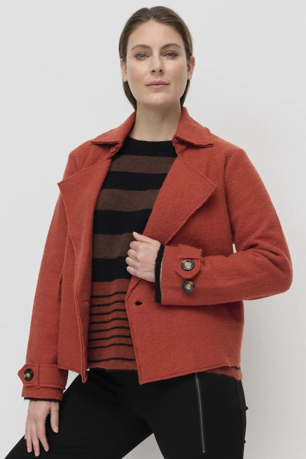 Woman wearing a rust coat over a striped shirt on a white background